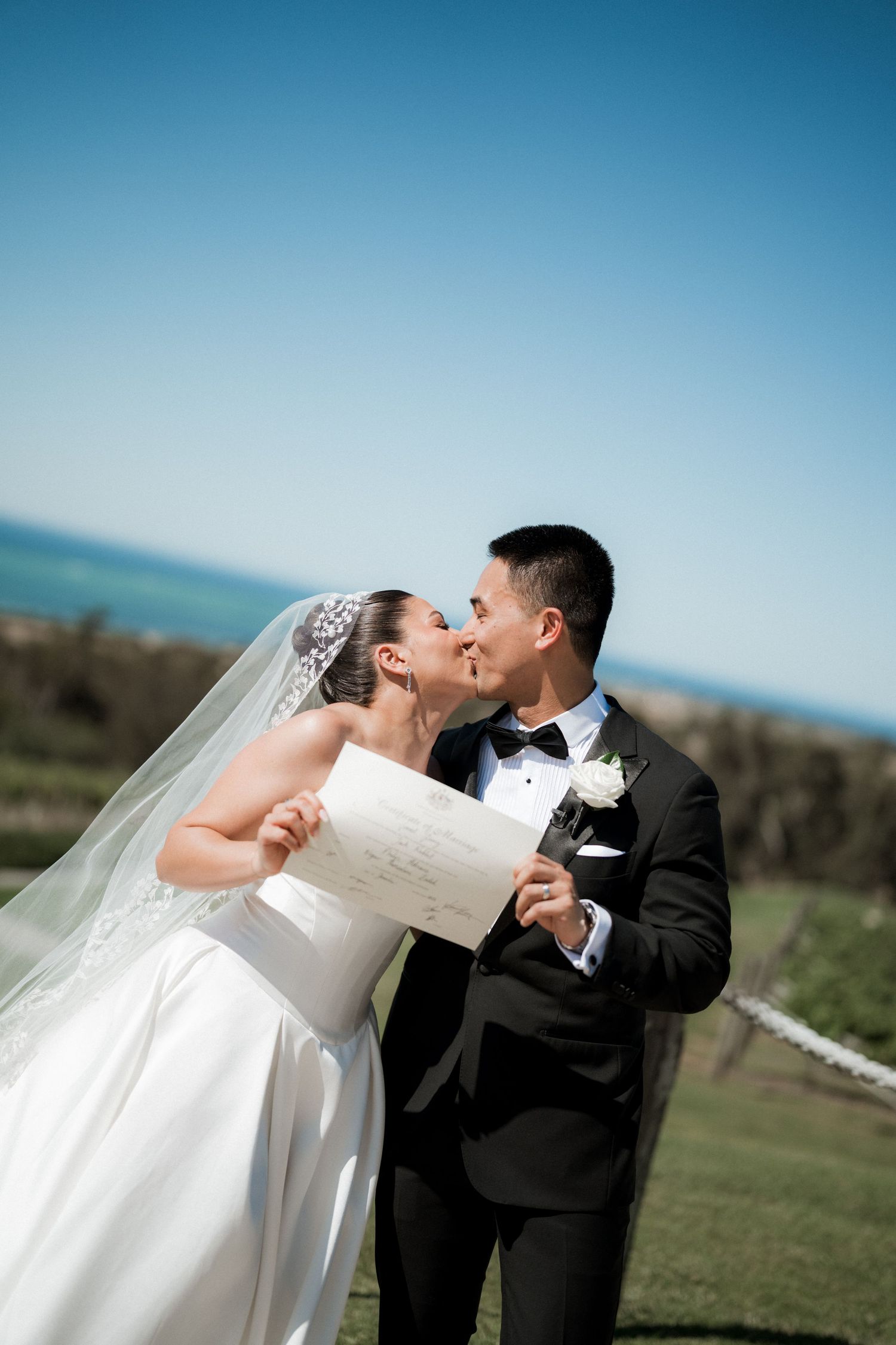 Wedding couple embraces outdoors against blue sky and mountain landscape.