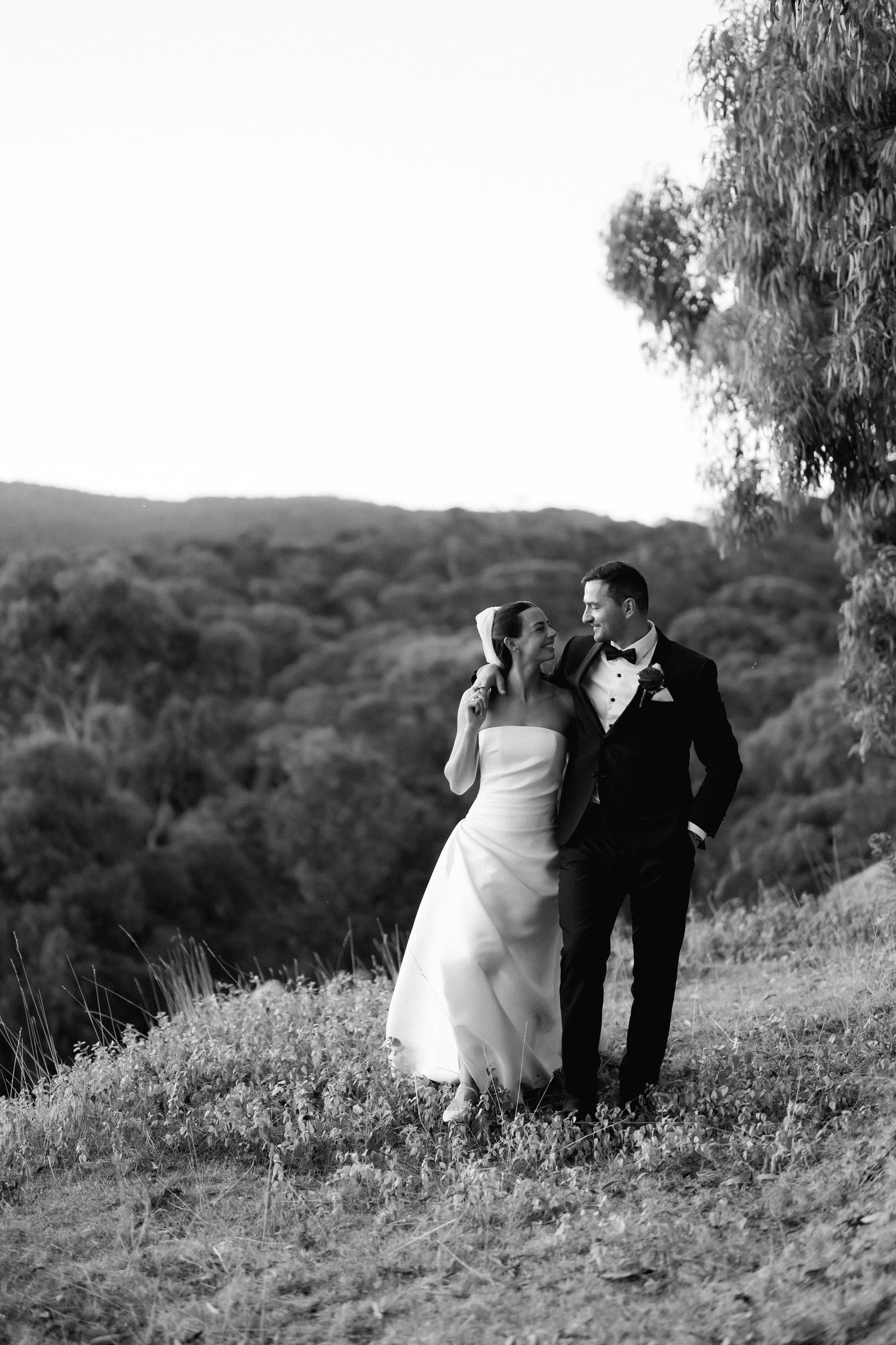 Black and white photo of a couple walking along a hilltop during their wedding.