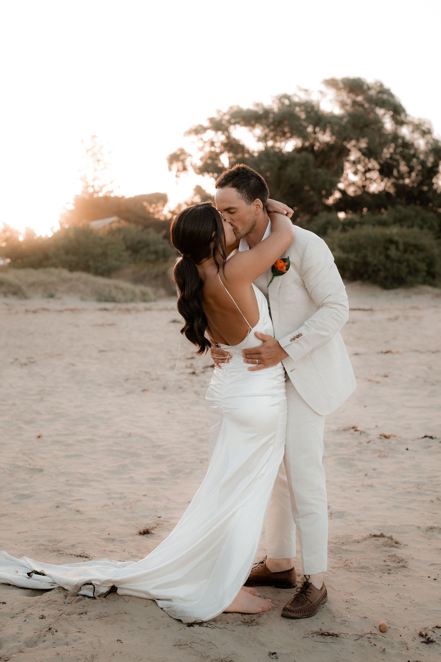 Romantic beach wedding photos at sunset with couple in white attire.