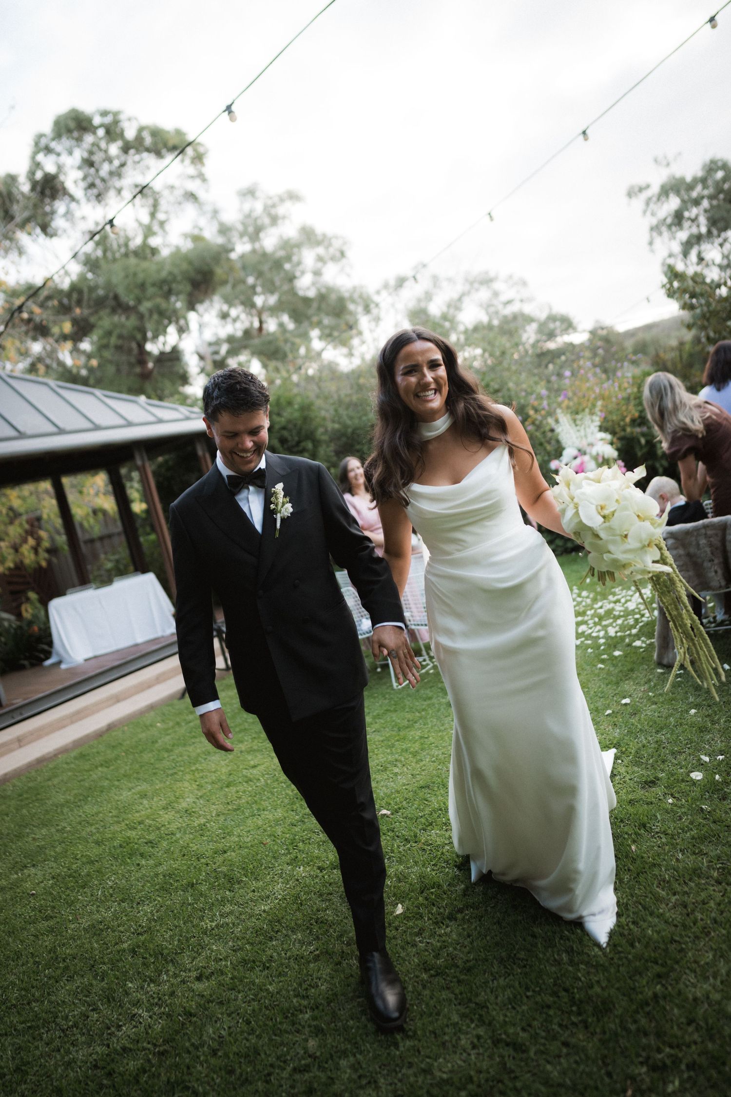 Joyful couple walking together on grass during outdoor wedding celebration.