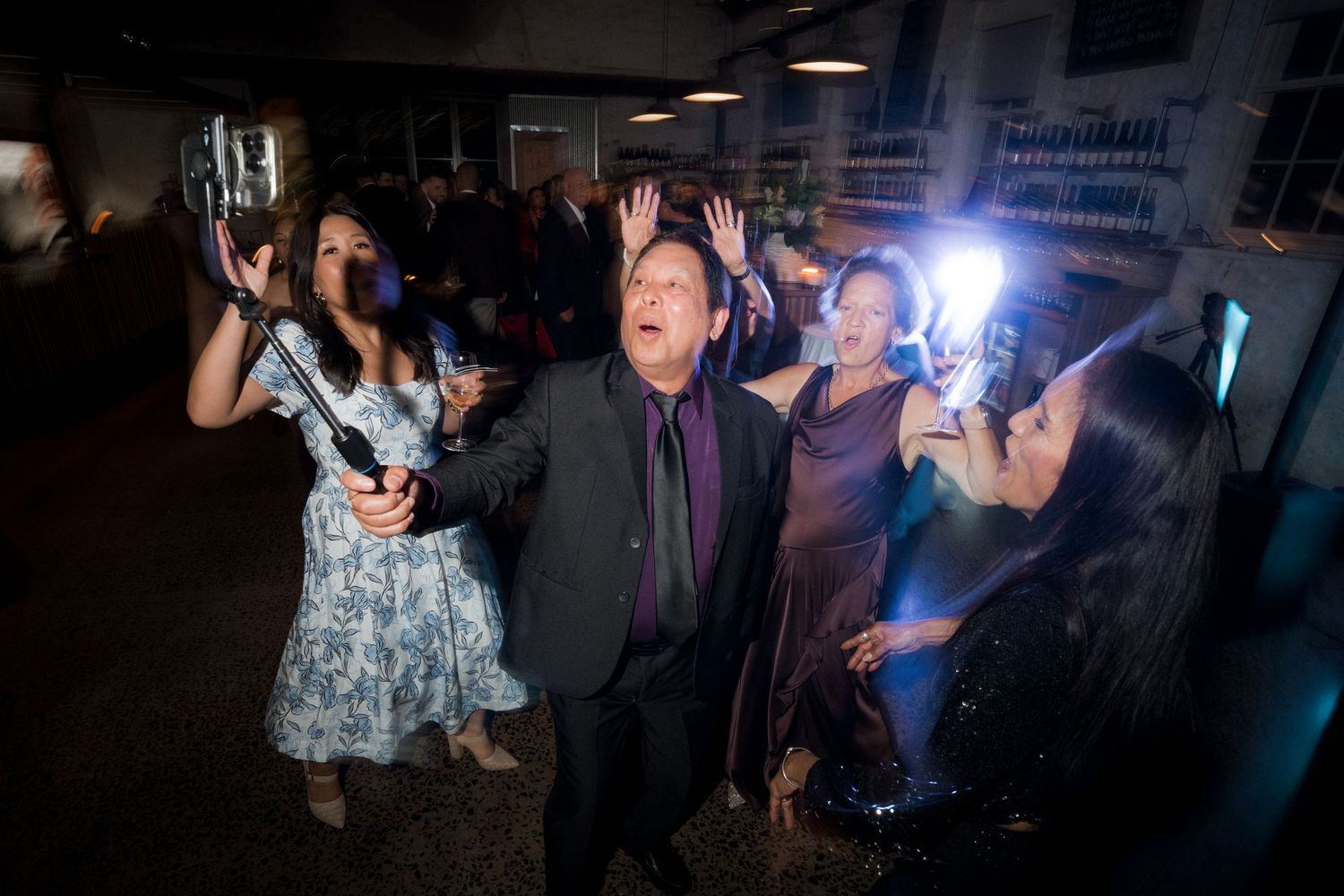 People dancing and celebrating on a dimly lit dance floor at a party with blue lighting effects.