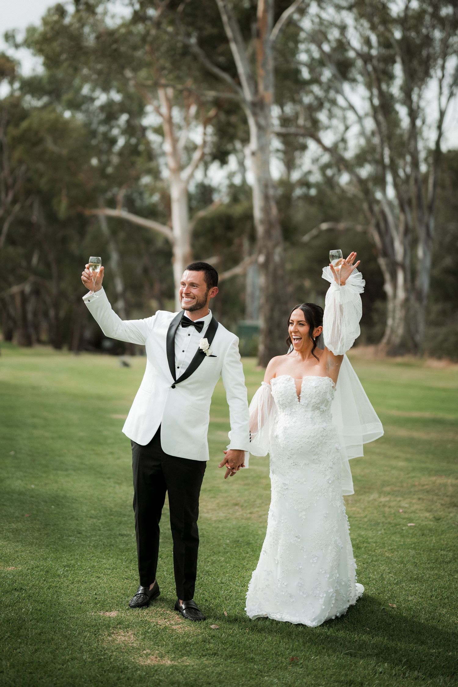 Wedding couple dancing and twirling playfully on a grassy field with eucalyptus trees in the background.