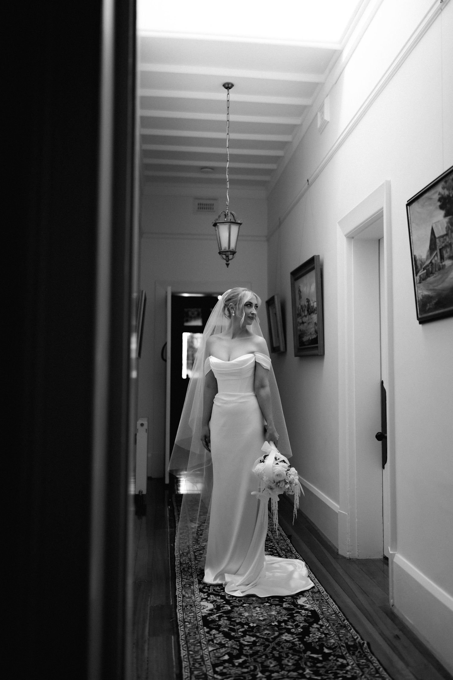 A white wedding dress hangs elegantly in a hallway with classic architectural details and framed artwork.
