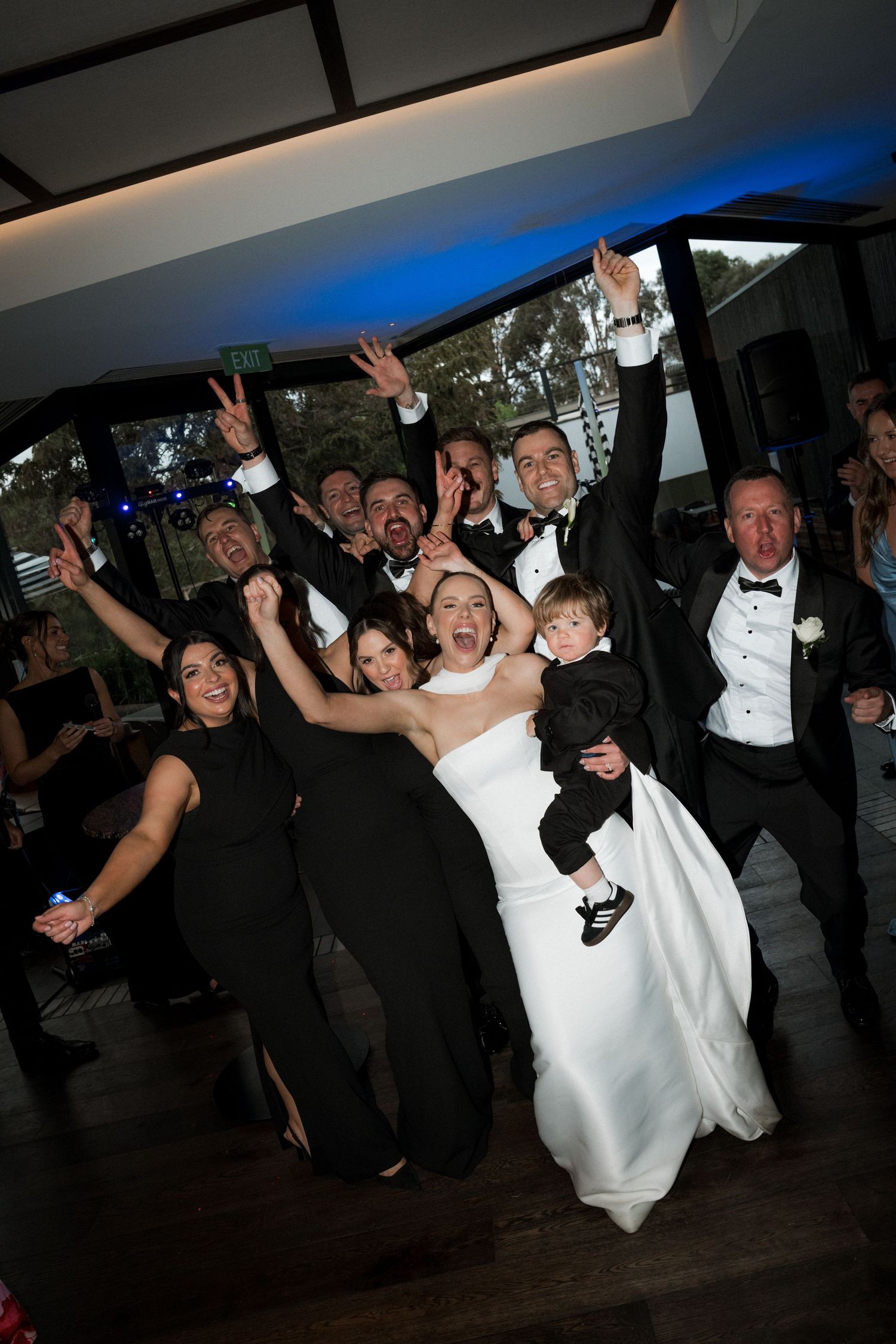 Wedding party celebrates on dance floor with energetic jumping and raised arms.
