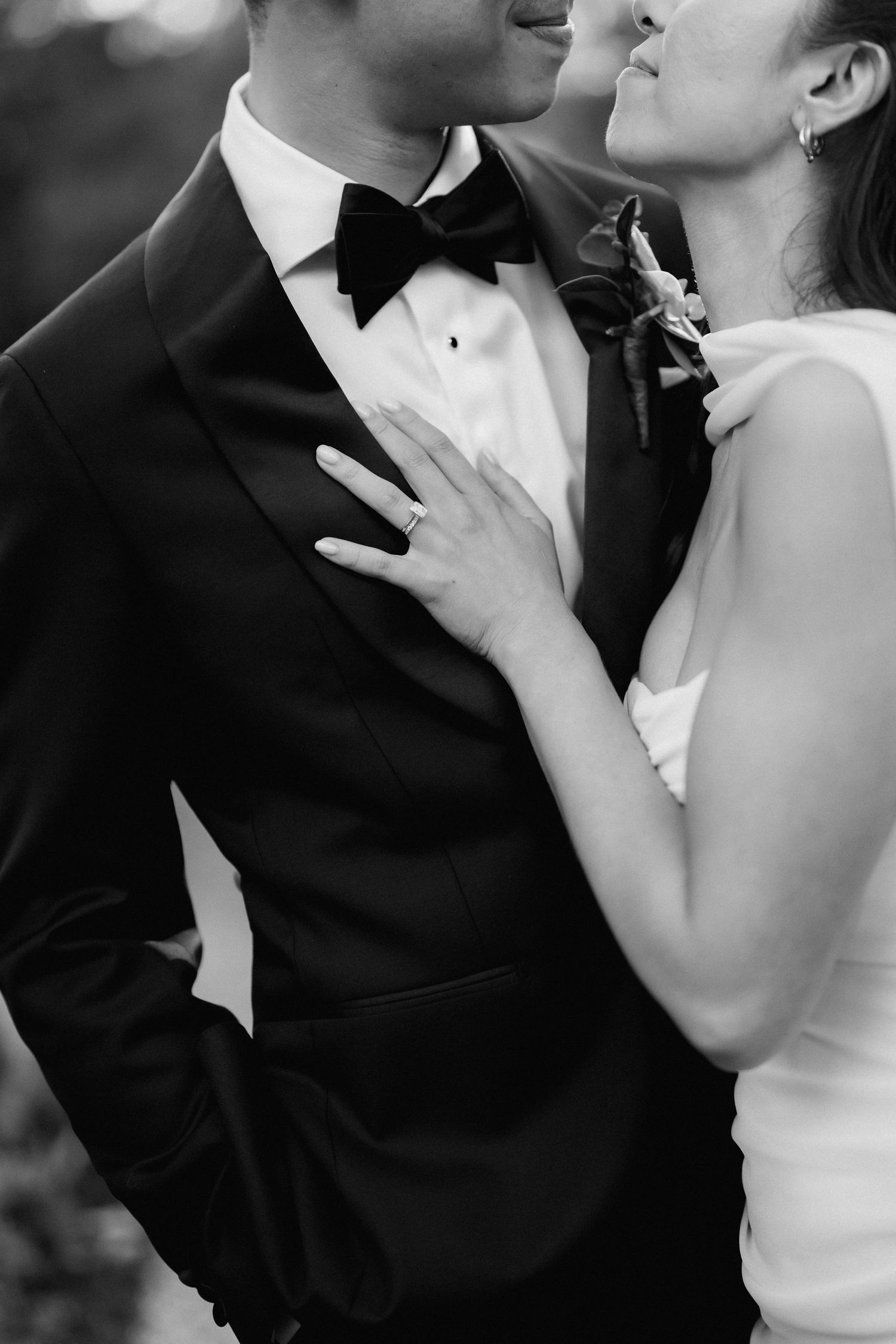 Black and white photo of bride placing hand on grooms tuxedo chest at wedding.