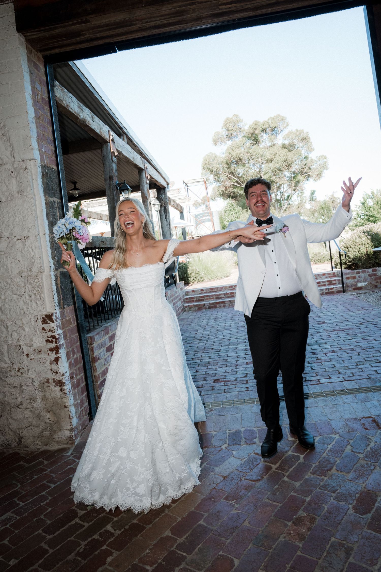 Joyful bride and groom celebrating at rustic brick wedding venue entrance.