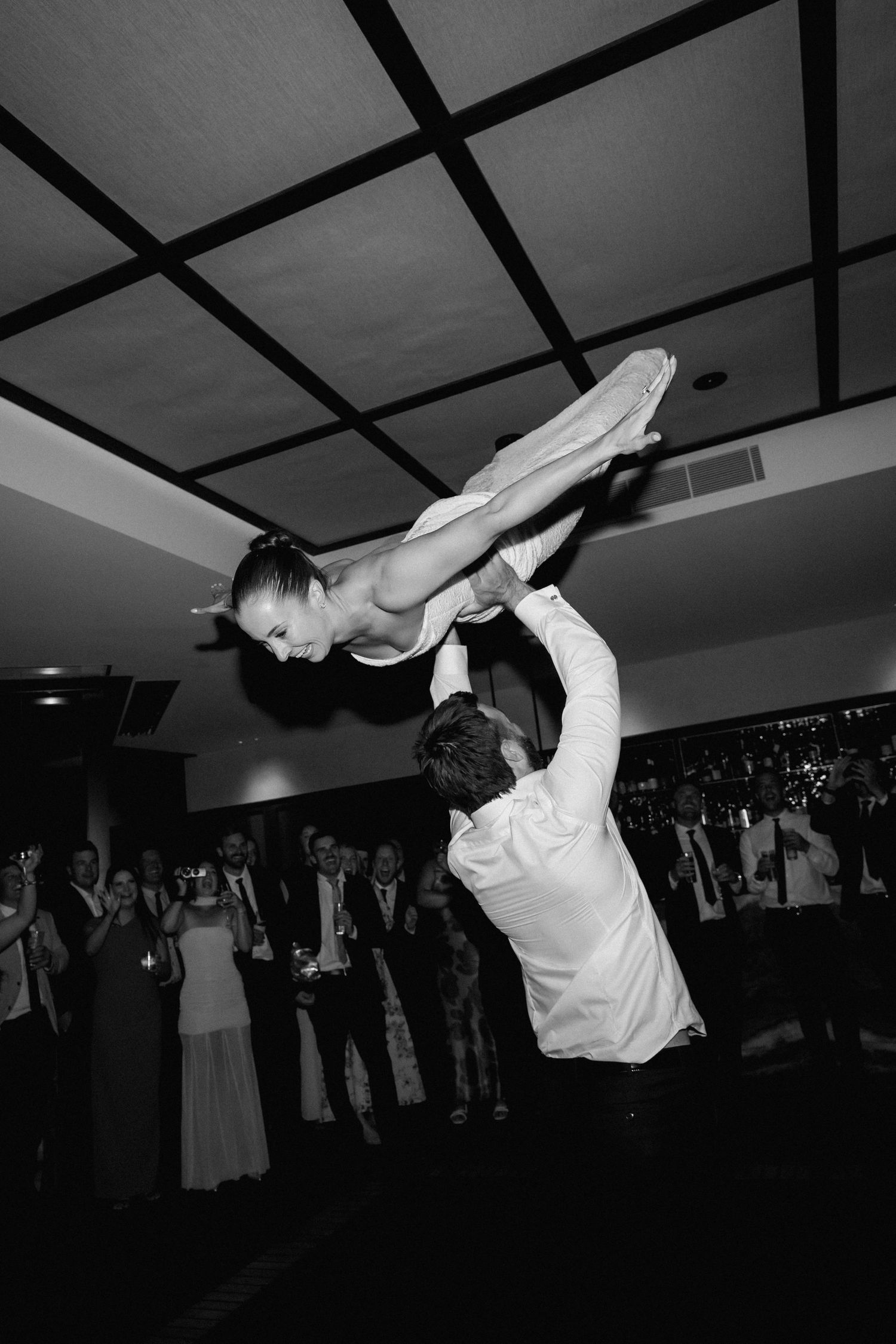 A bride and groom perform an impressive acrobatic lift during their first wedding dance while guests watch in amazement.