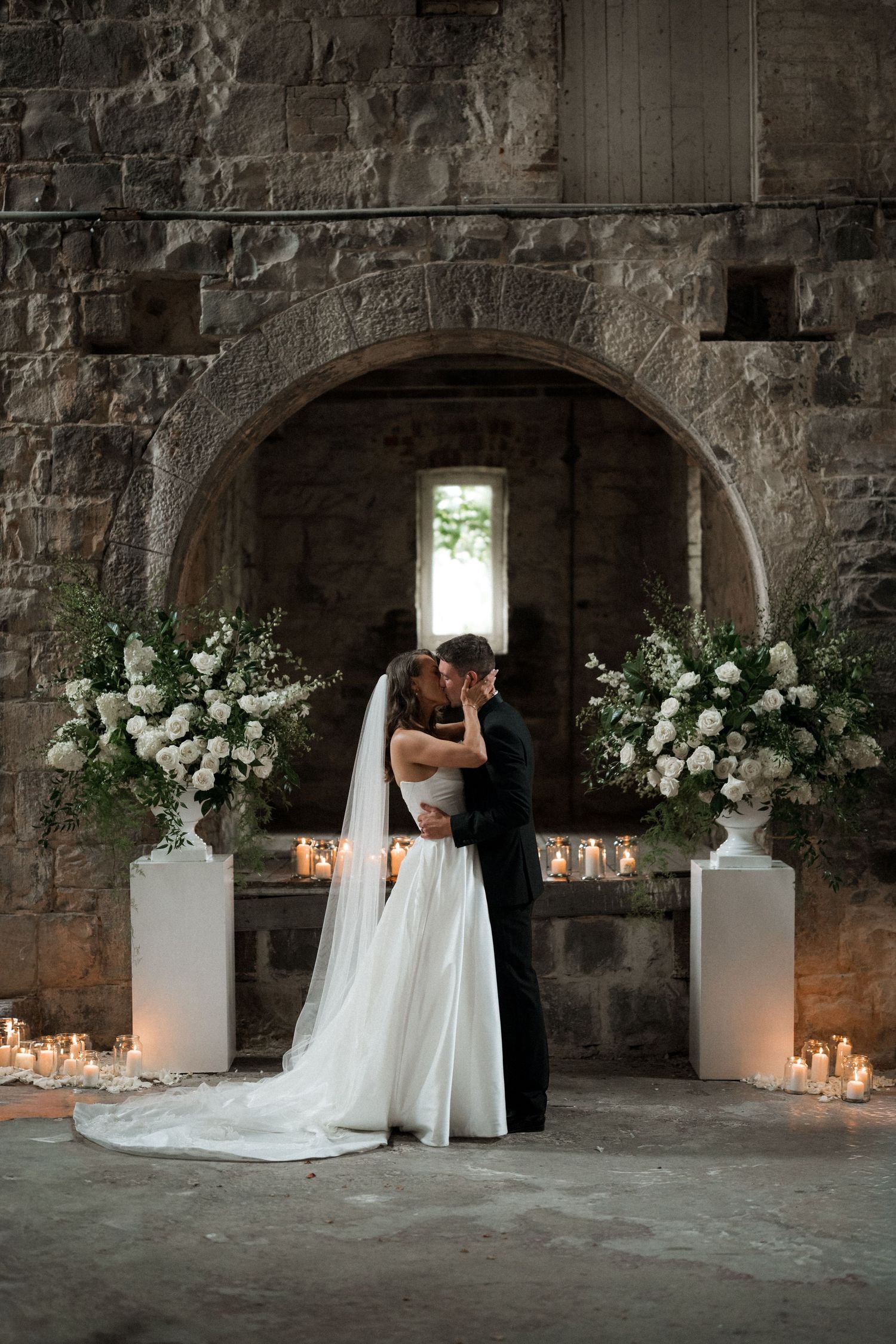 A romantic wedding scene in a stone castle cellar with white floral arrangements and glowing candles.