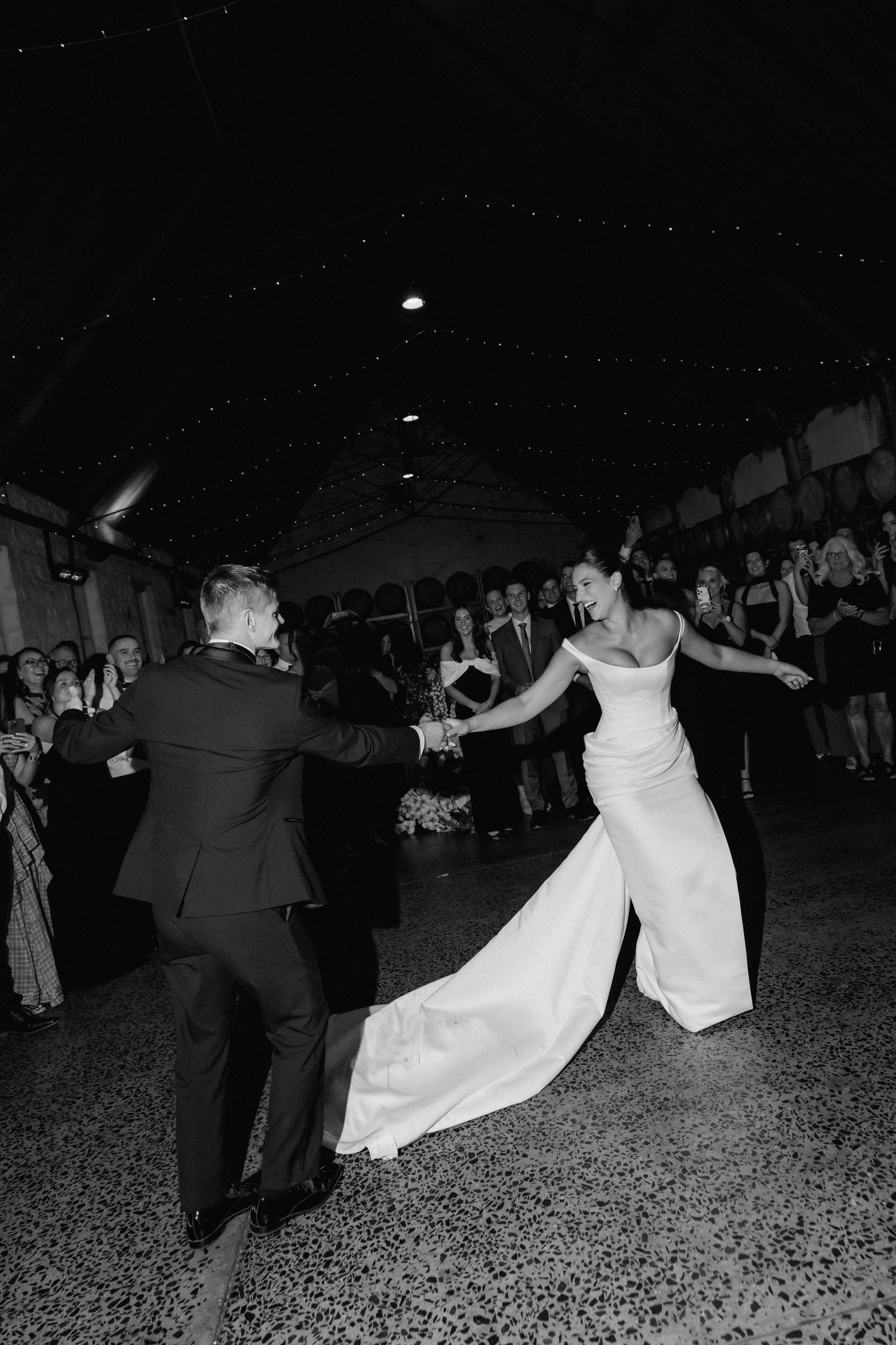 Wedding guests dance together in a lively reception celebration captured in black and white.