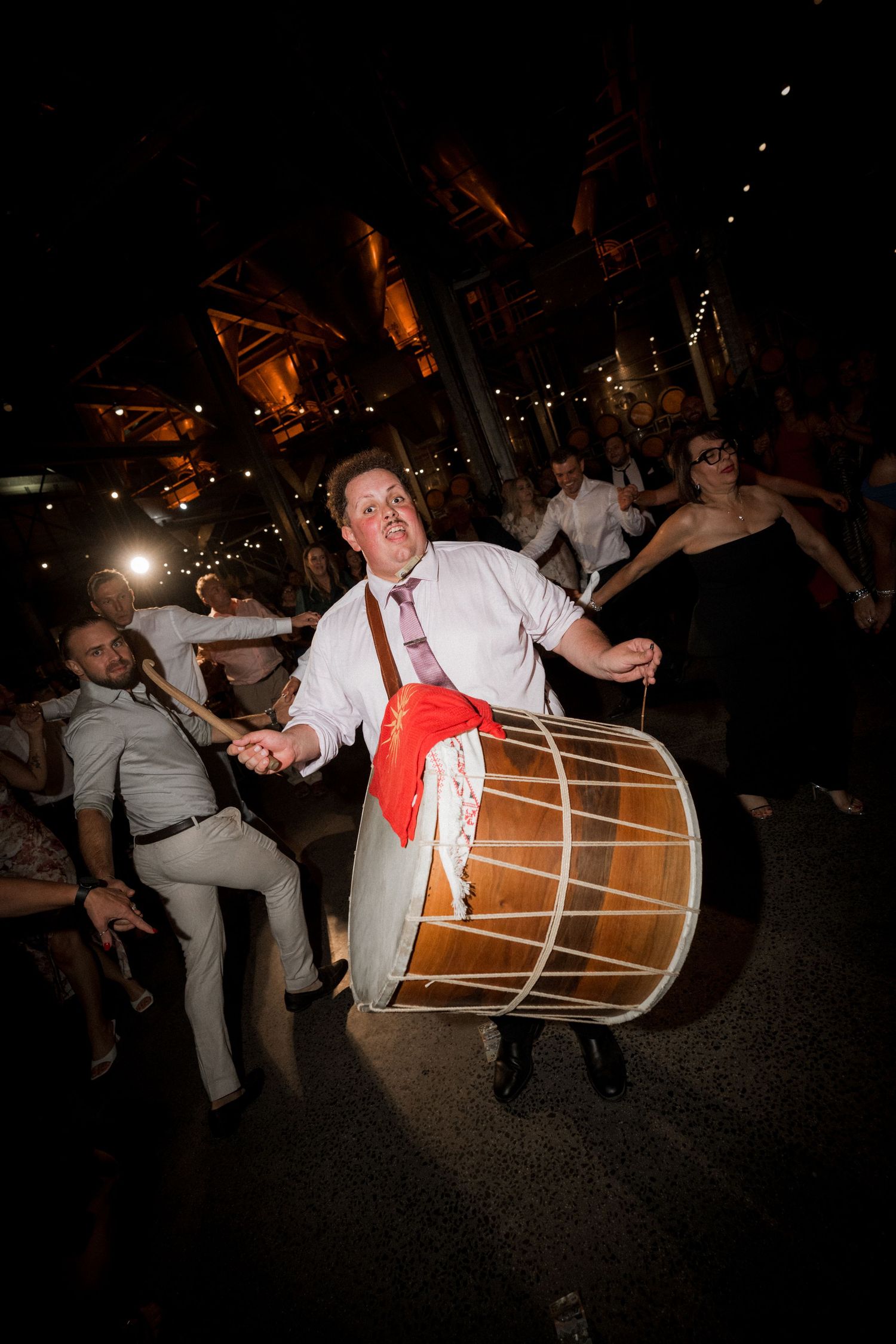 A drummer performs enthusiastically with a large bass drum at a lively nighttime celebration.