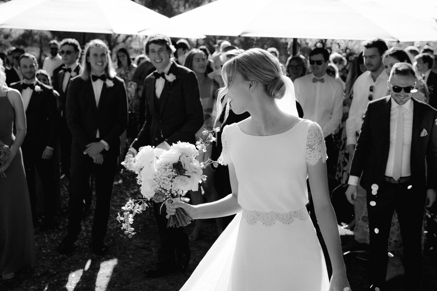 Black and white photograph of an outdoor wedding celebration with guests gathered under a tent.