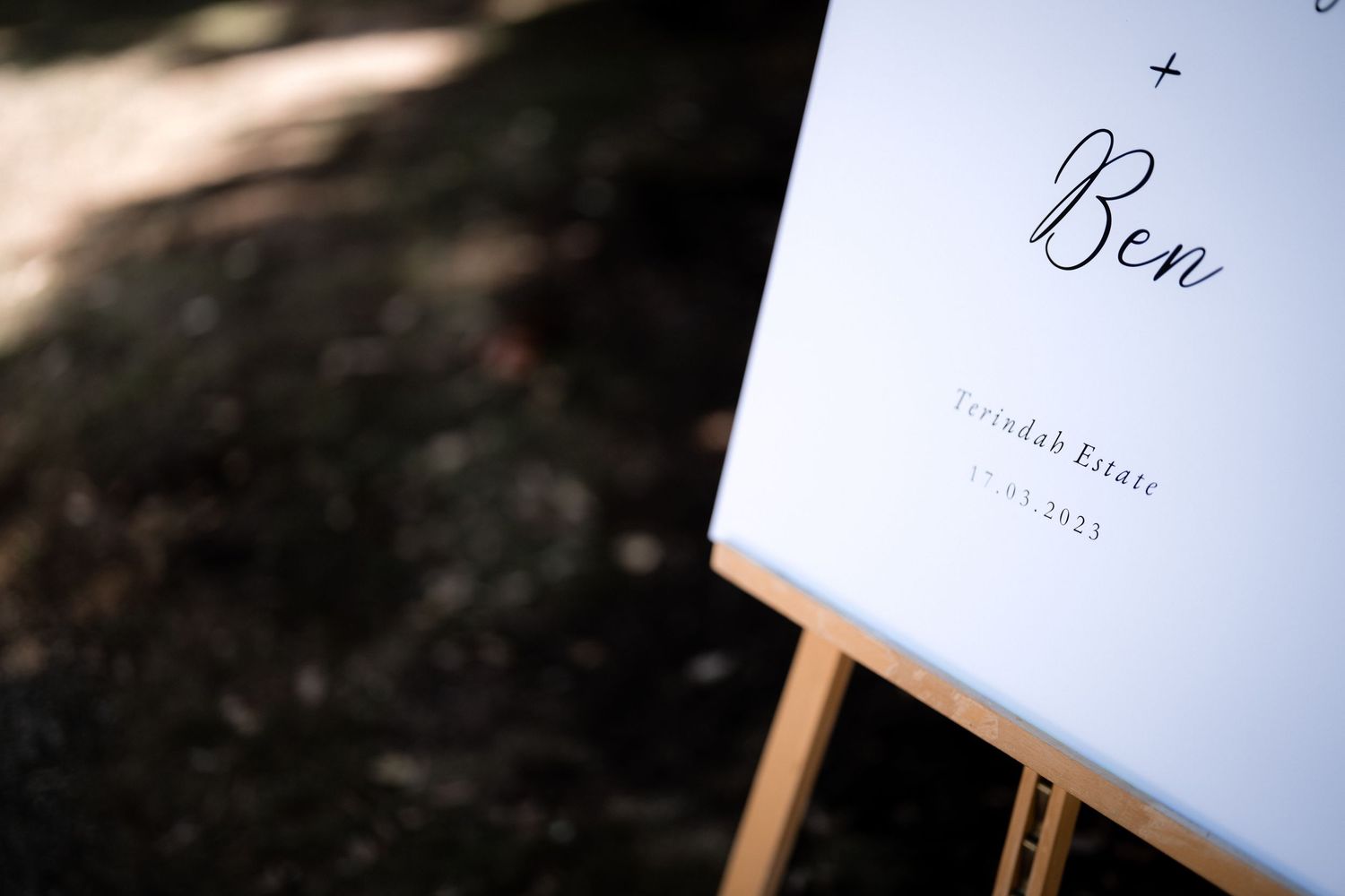 A wedding sign with the name 'Ben' displayed on a white board mounted on a wooden easel.