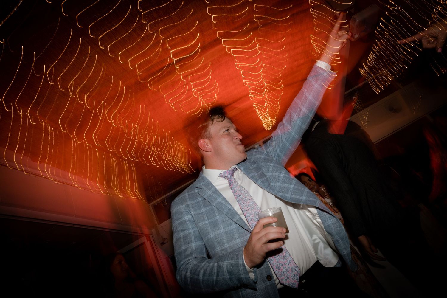 A party guest dances energetically beneath red-lit geometric light patterns at a celebration.
