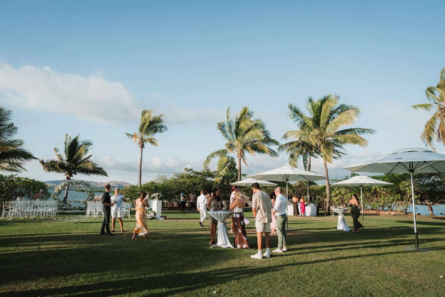 Wedding guests gathered on a palm-lined lawn during an outdoor reception.