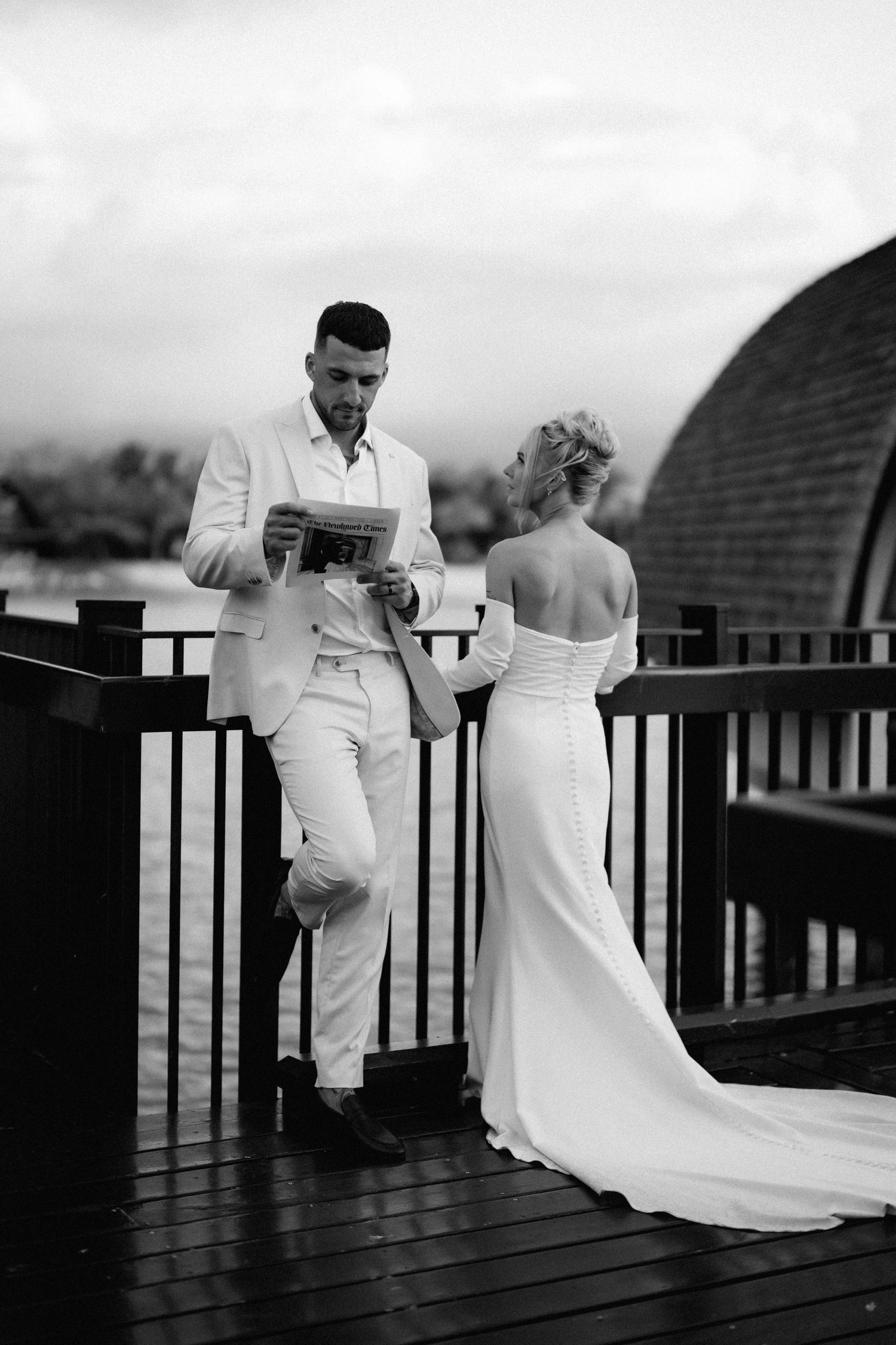 Black and white photo of a couple on a wooden deck with dramatic architectural backdrop.