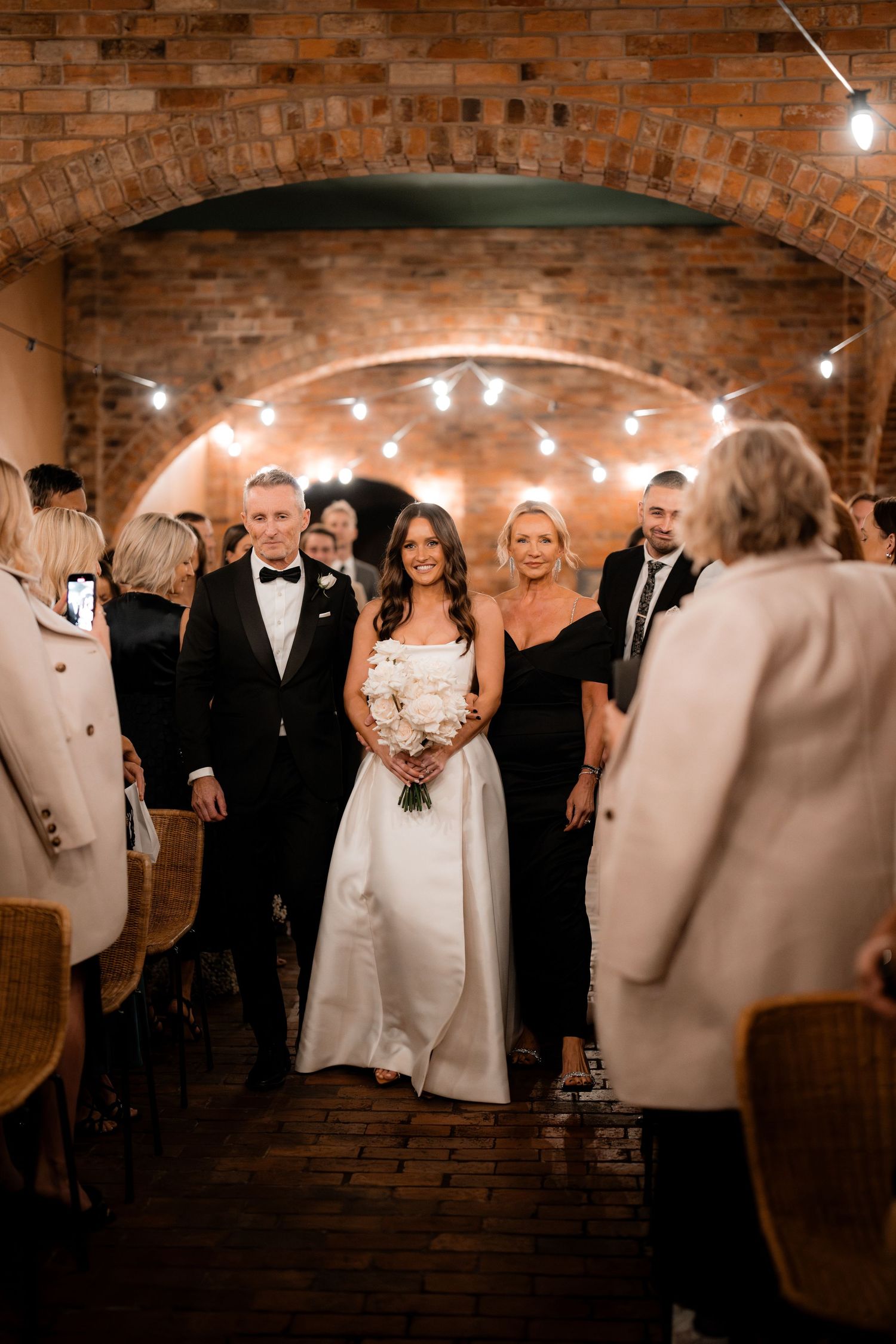 Wedding party gathers in an elegant brick-walled venue with ambient lighting.