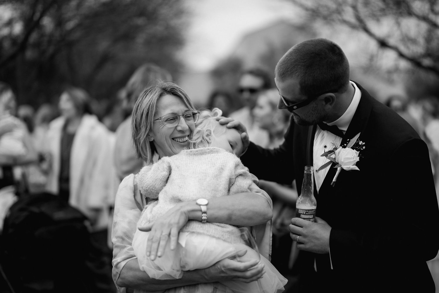 A couple shares a joyful moment while holding something small wrapped in white at an outdoor gathering.