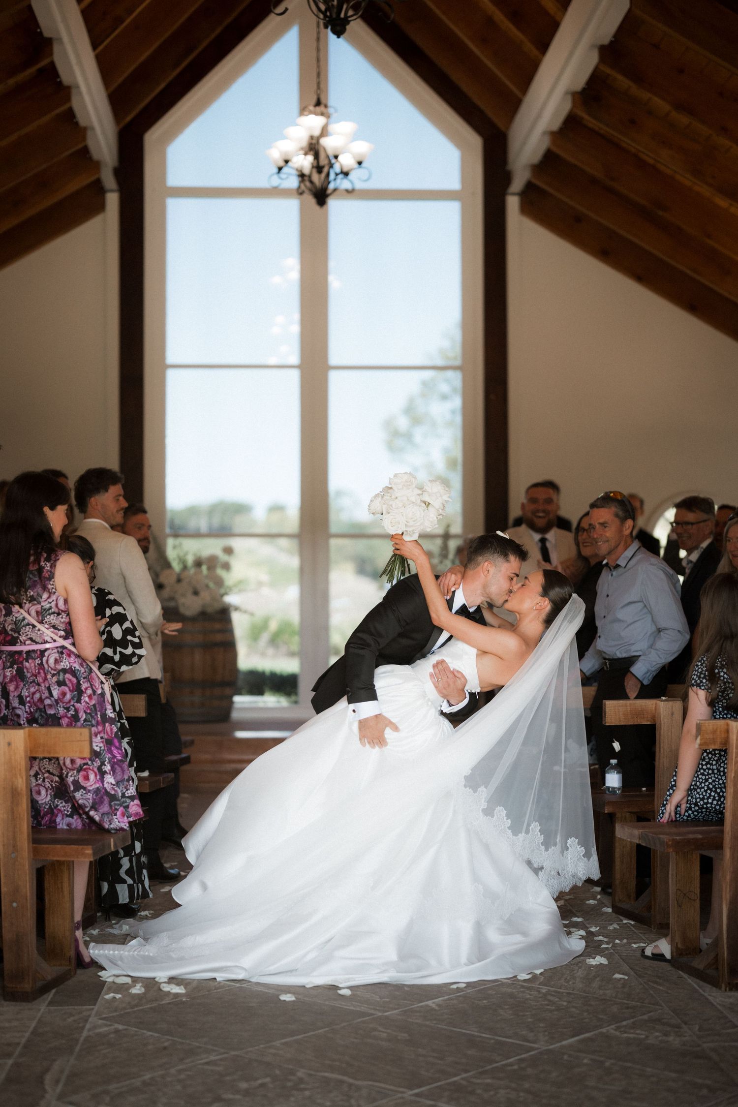 A romantic dip pose during a wedding ceremony in a rustic chapel with wooden beams.