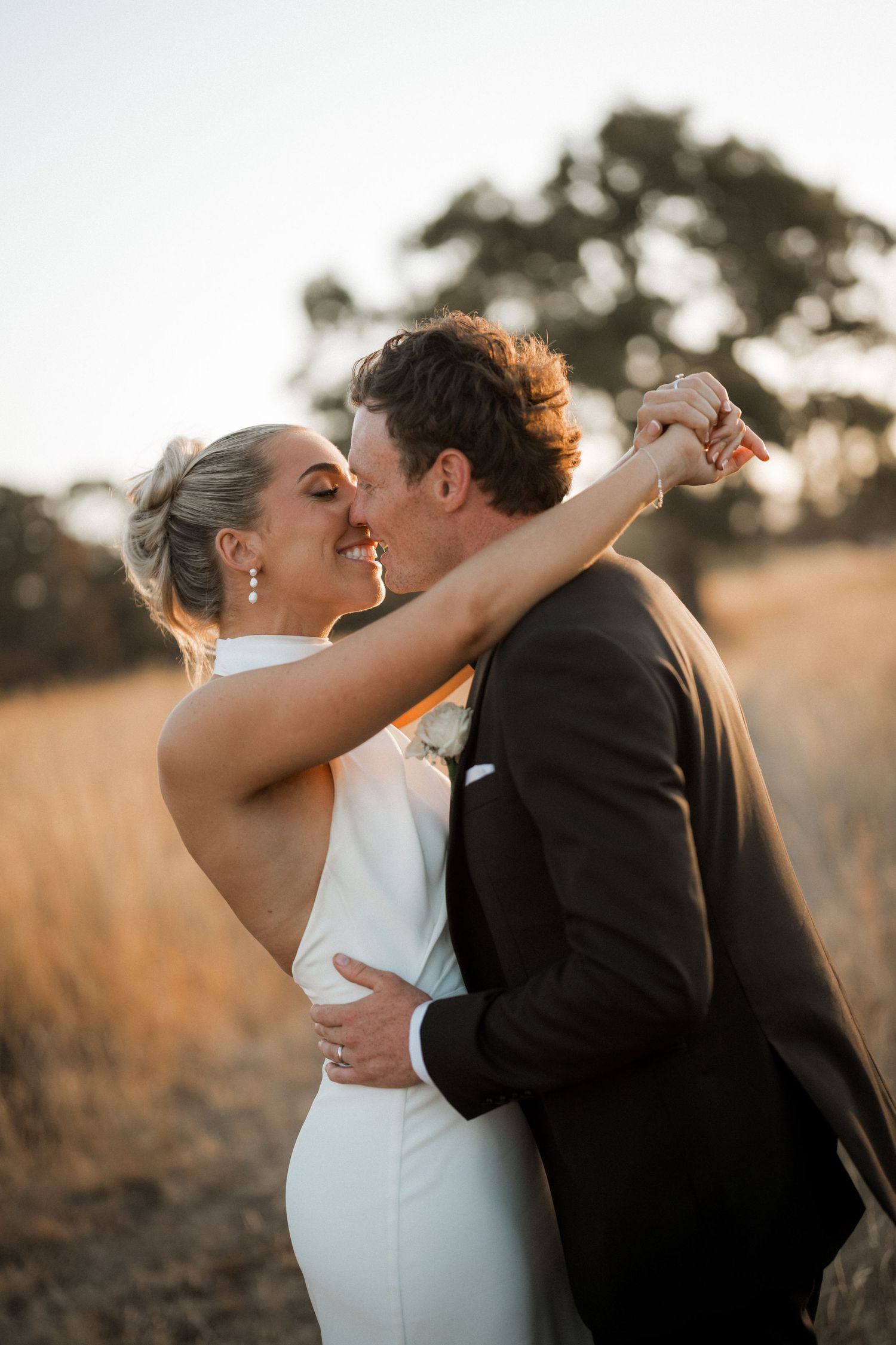 Romantic sunset portrait of newlyweds embracing in golden field.