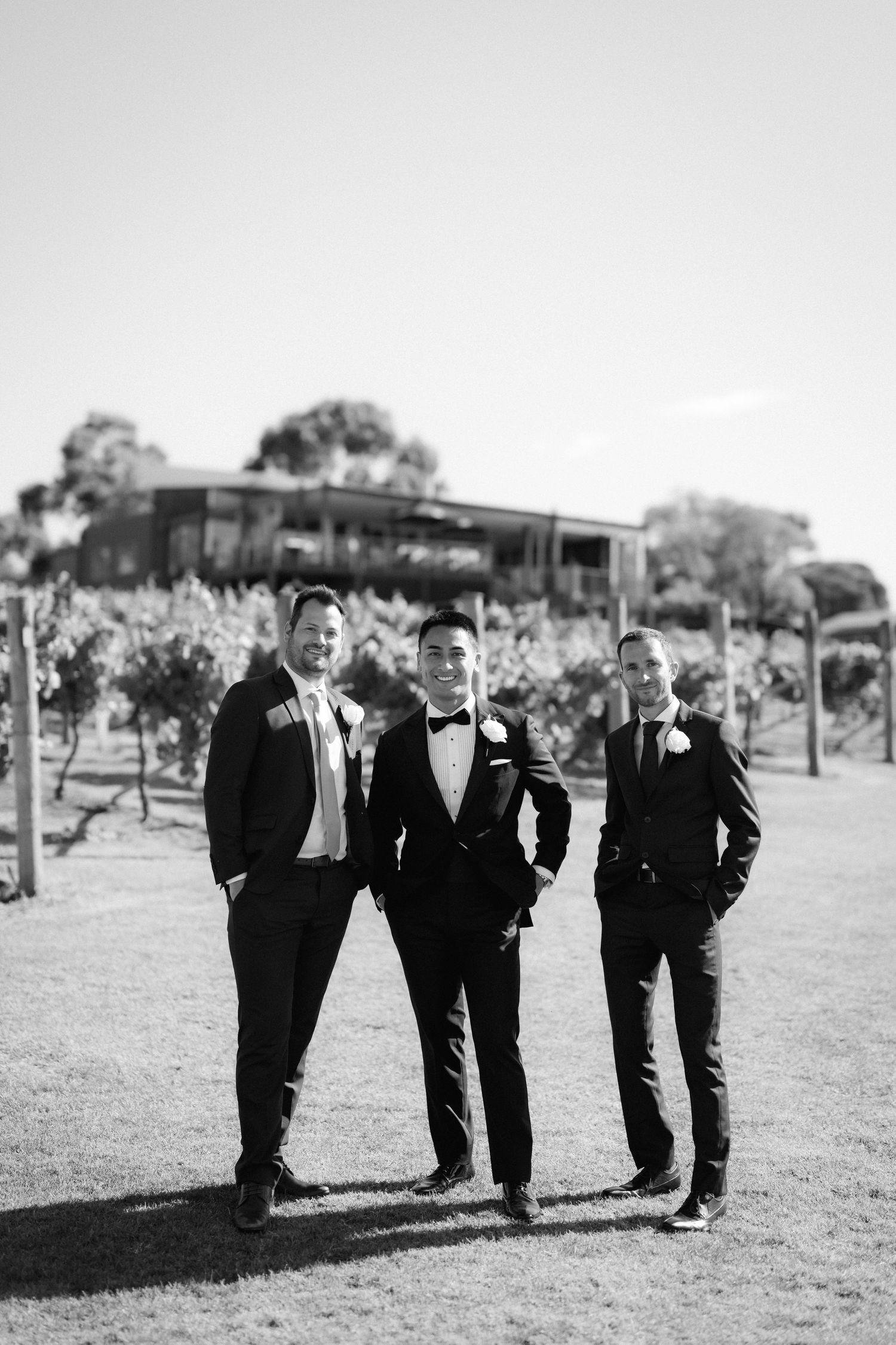 Groomsmen in black suits walk across a grassy field in black and white photography.