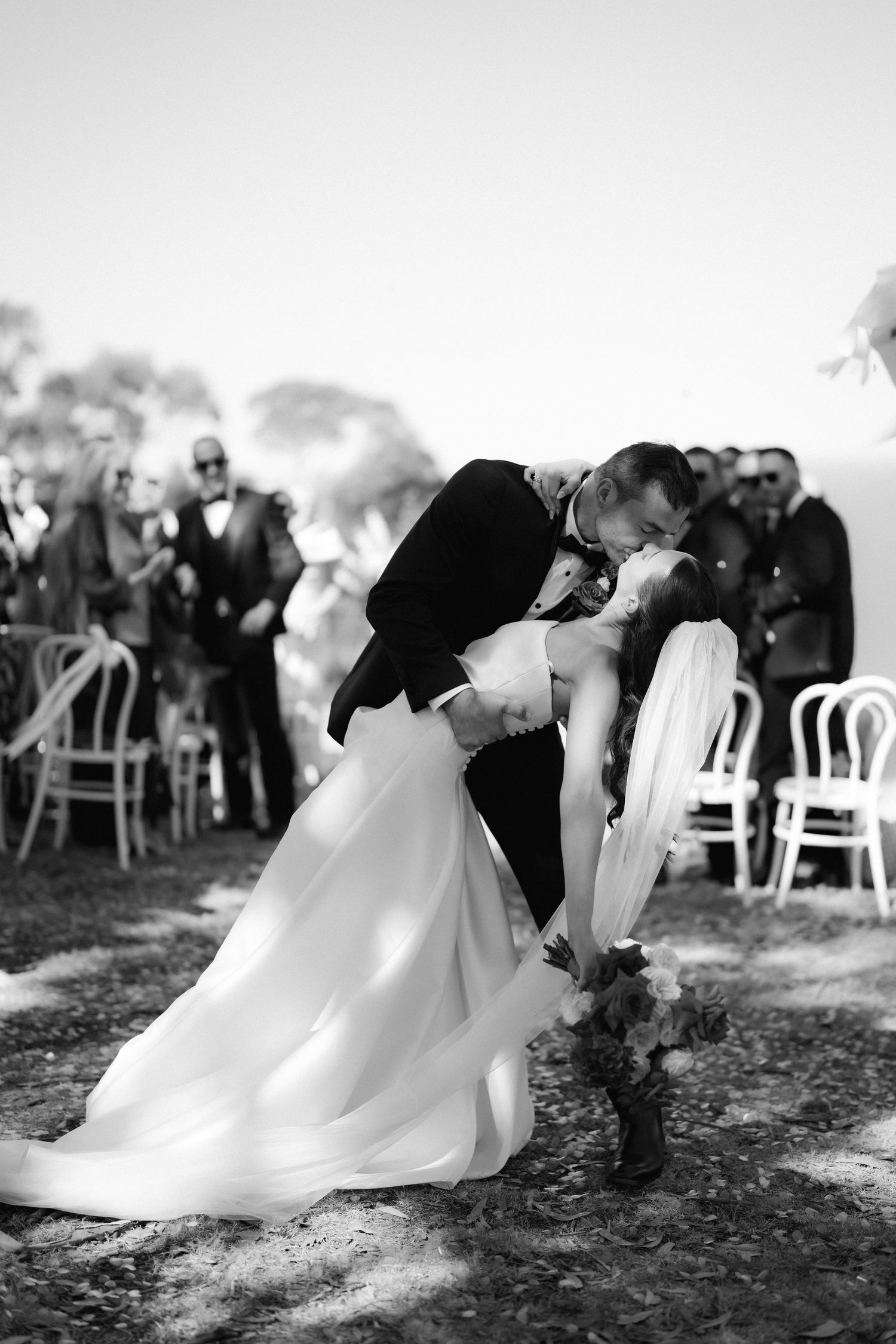 Dramatic black and white wedding photos showing romantic dip poses with guests in background.