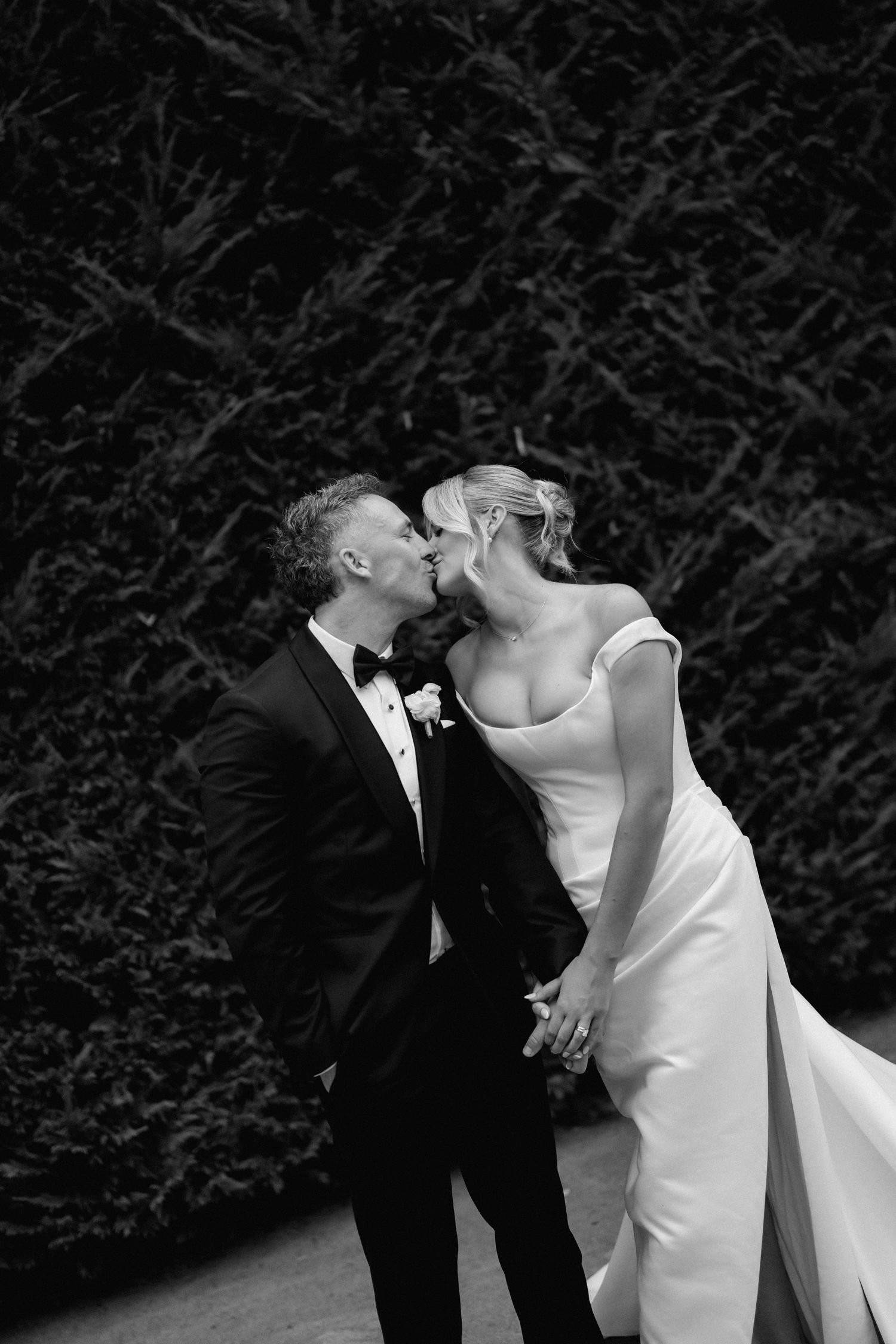 A romantic black and white wedding photo series showing a couple embracing against a dark hedge background.