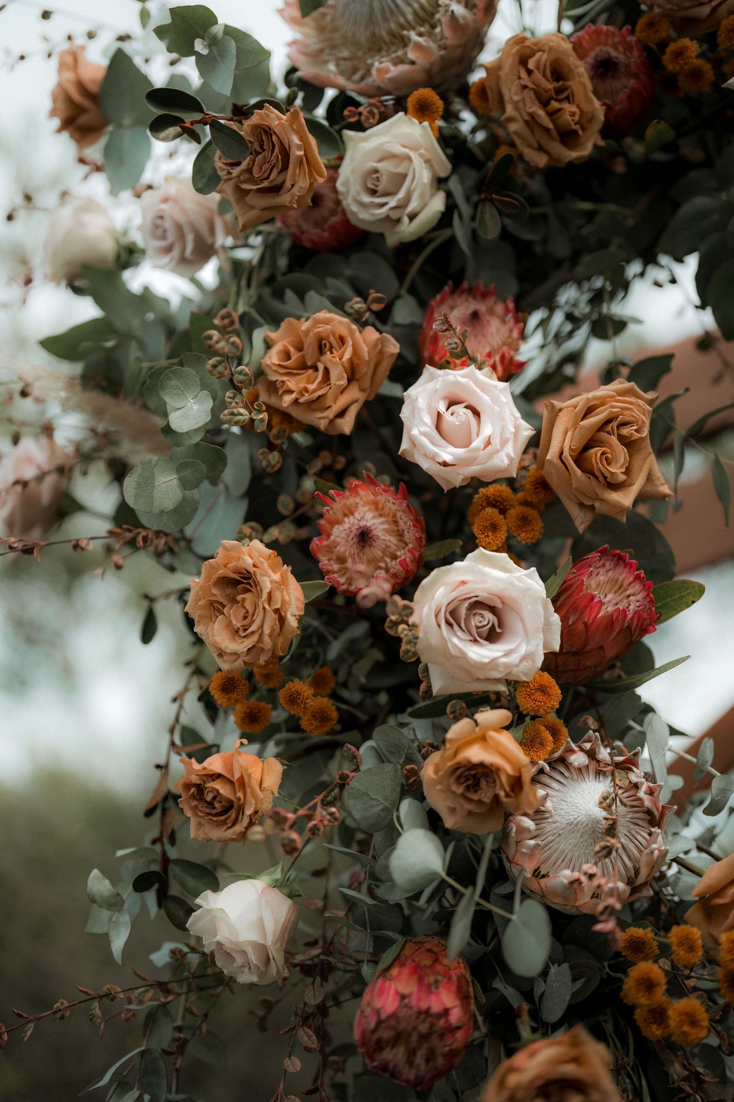 Moody floral arrangement of dried and fresh roses in shades of rust, peach and cream with eucalyptus foliage.