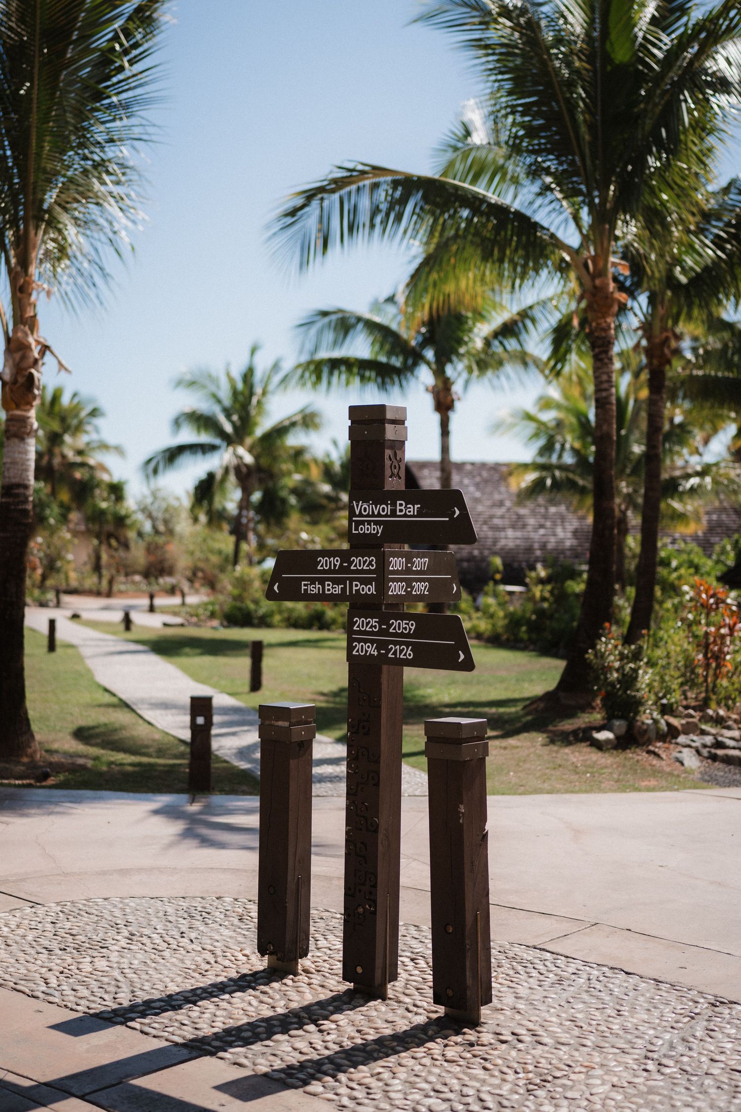 Wooden directional signpost surrounded by palm trees at a tropical resort walkway.