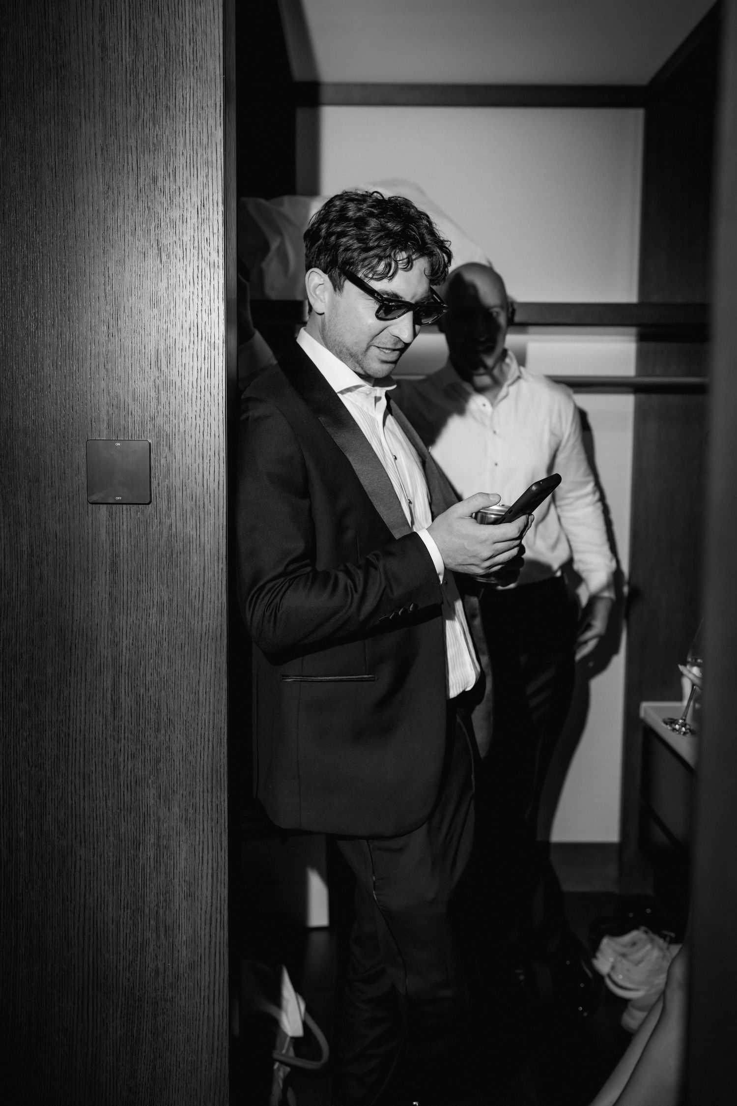 Person in formal attire checking phone in dimly lit hallway.