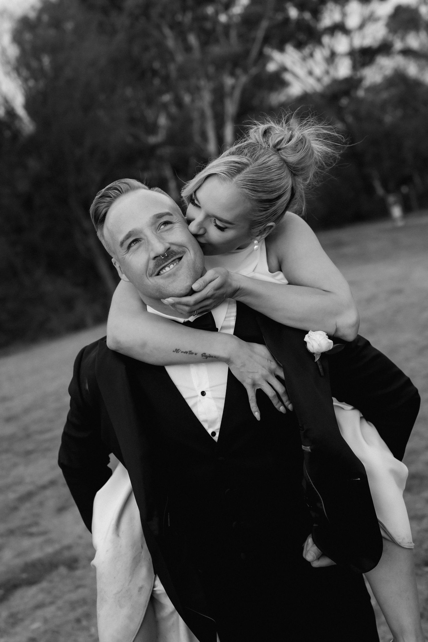 A joyful black and white wedding photo captures a candid moment between a couple as they share a playful embrace outdoors.