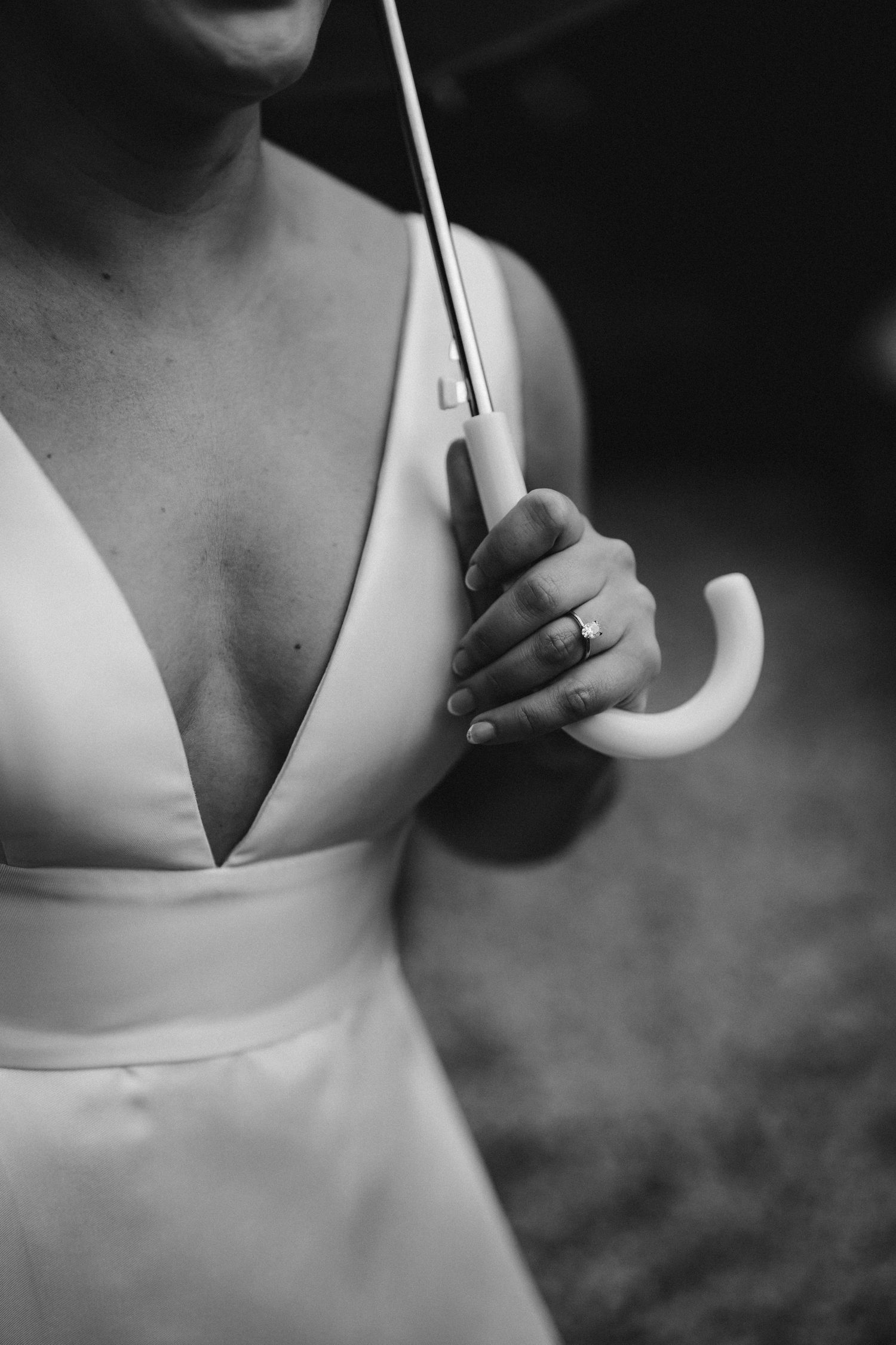 A close-up black and white photo showing hands holding a white umbrella handle against a dress with a plunging neckline.