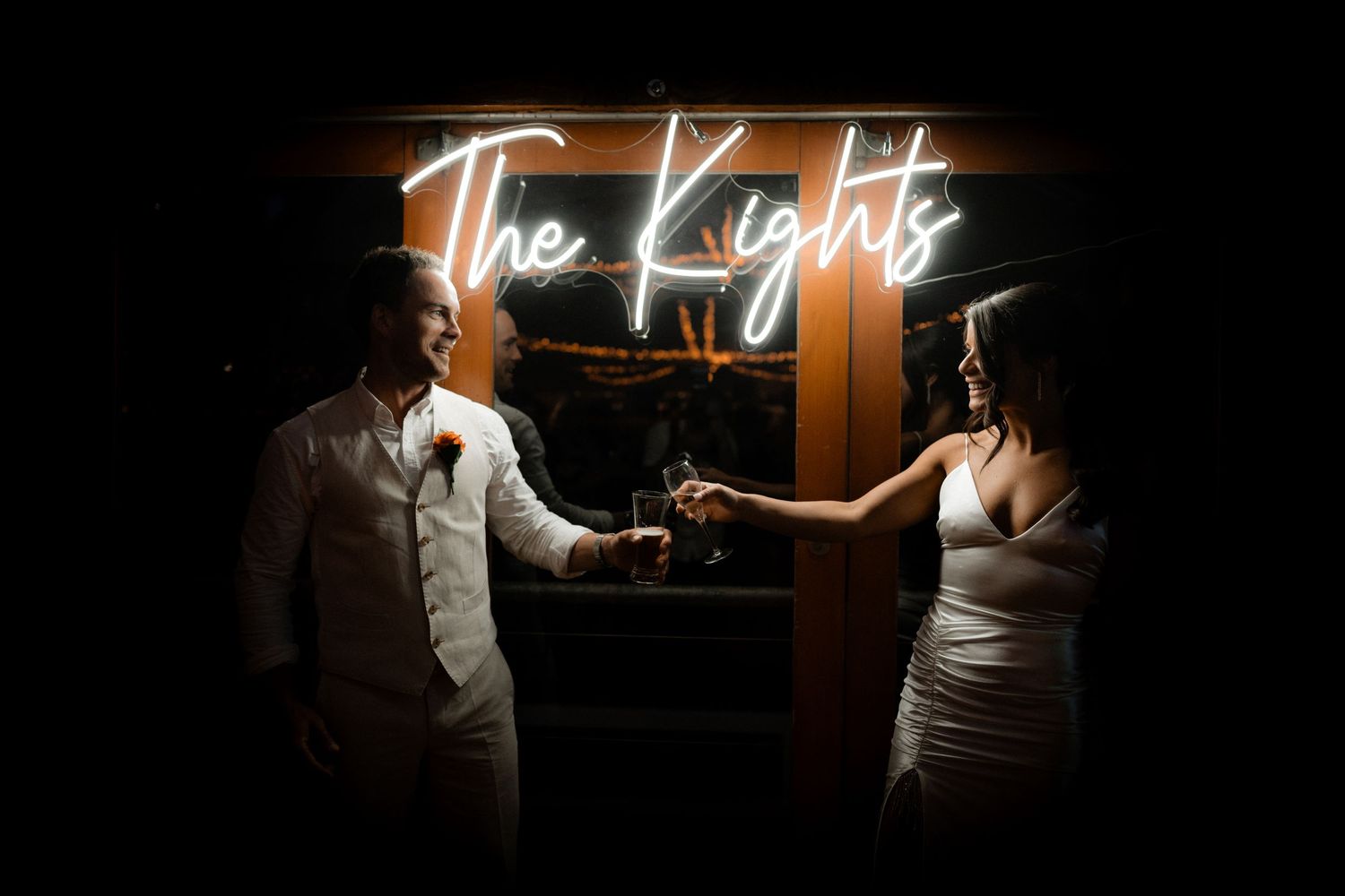 A dimly lit wedding reception scene with neon signage glowing in the background.