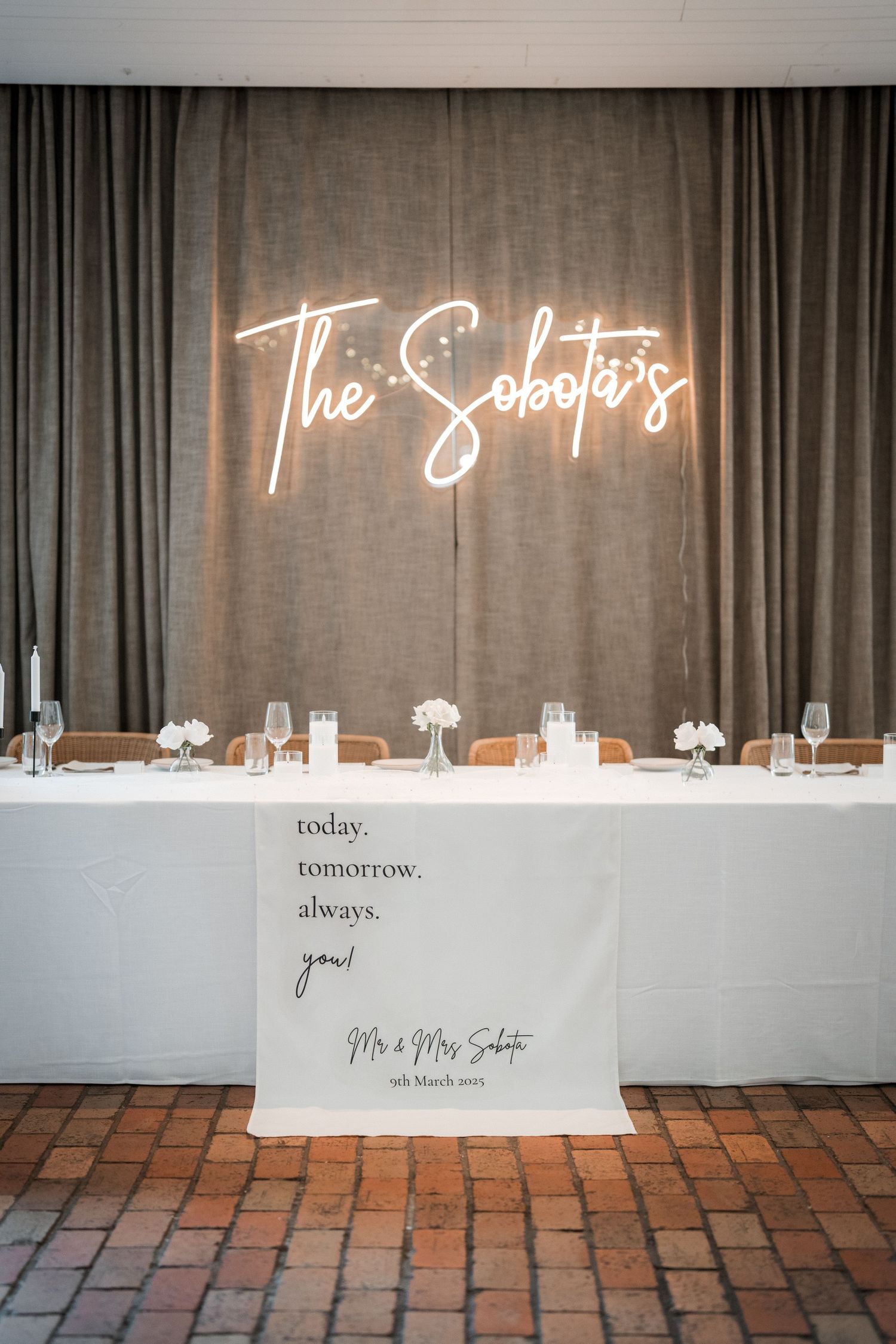 Elegant wedding reception decor with white tables and neon signs against a dark curtain backdrop.