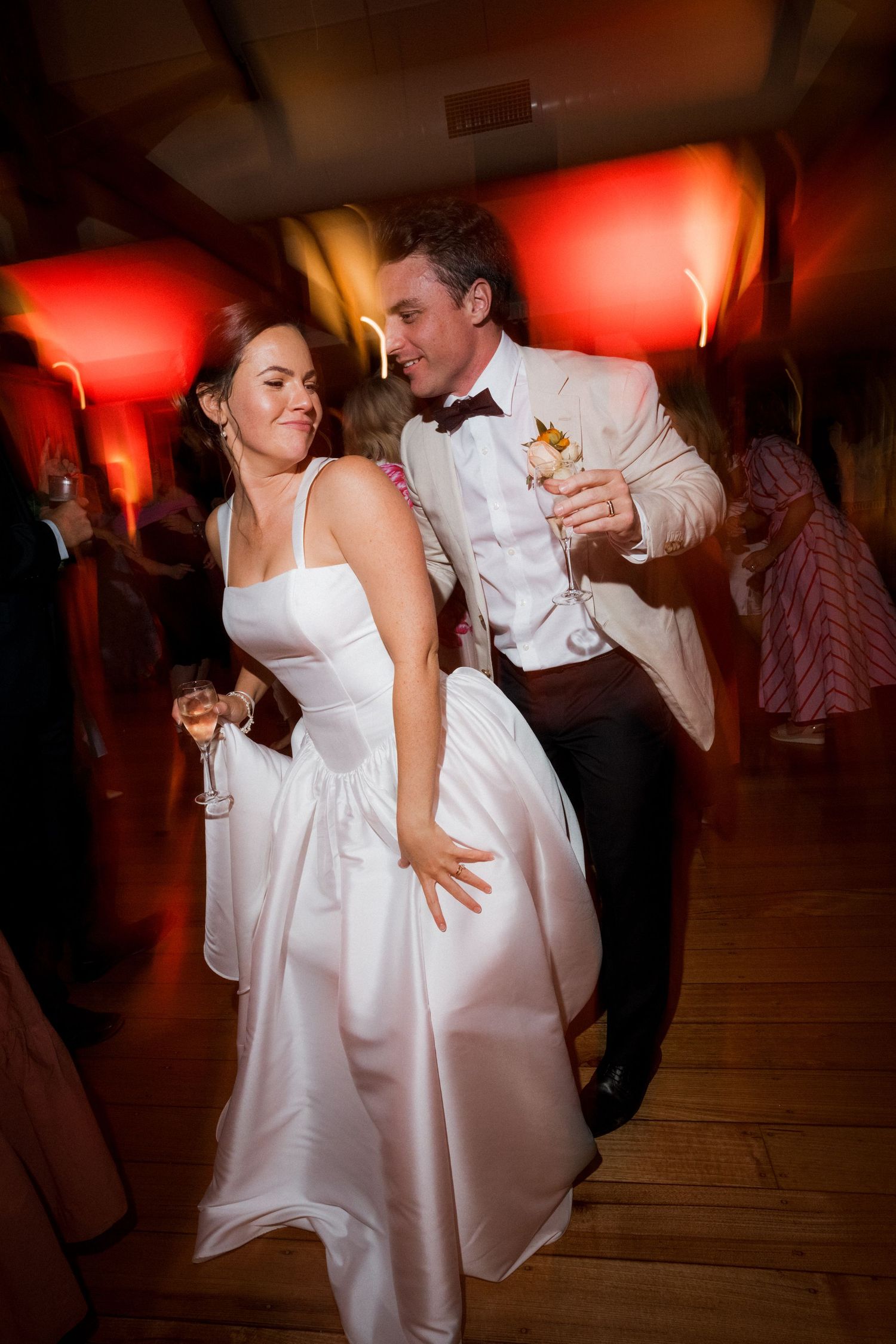 Wedding couple dancing in dramatic red lighting on a wooden dance floor.