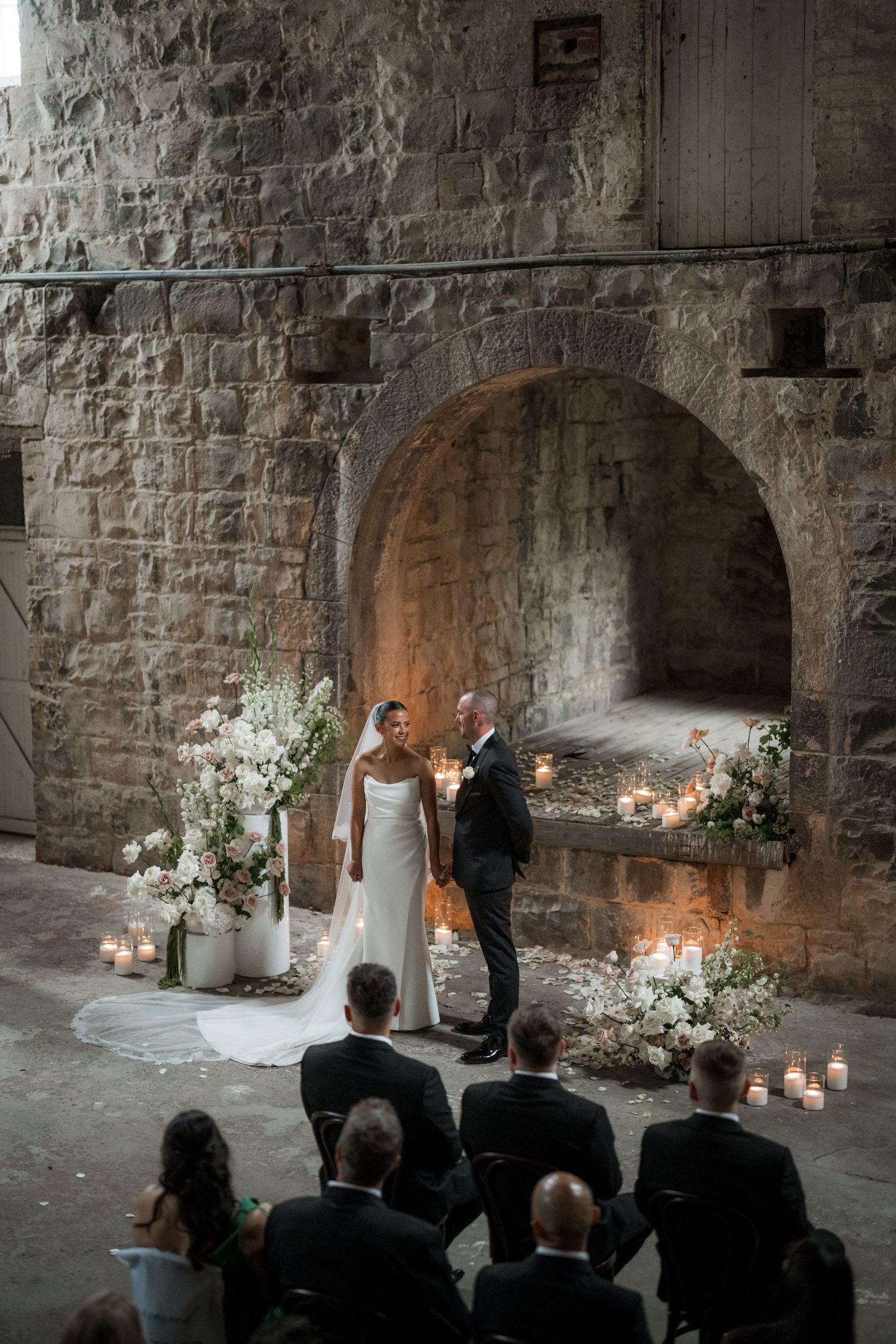 An intimate wedding ceremony in a rustic stone venue with candlelight and floral decorations.