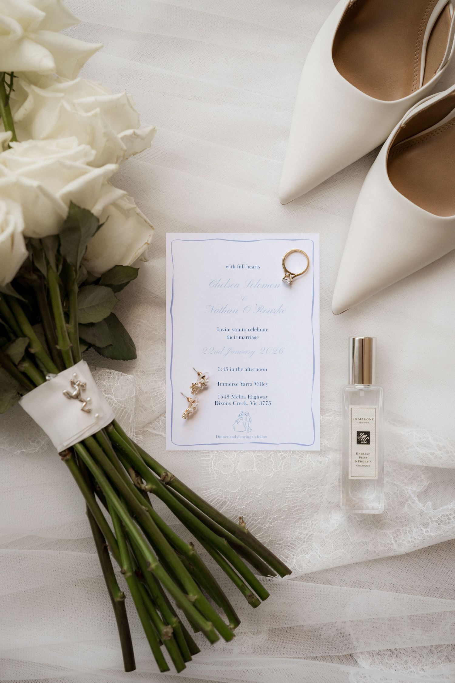 Wedding details including white roses, invitations, and elegant accessories arranged on a light surface.