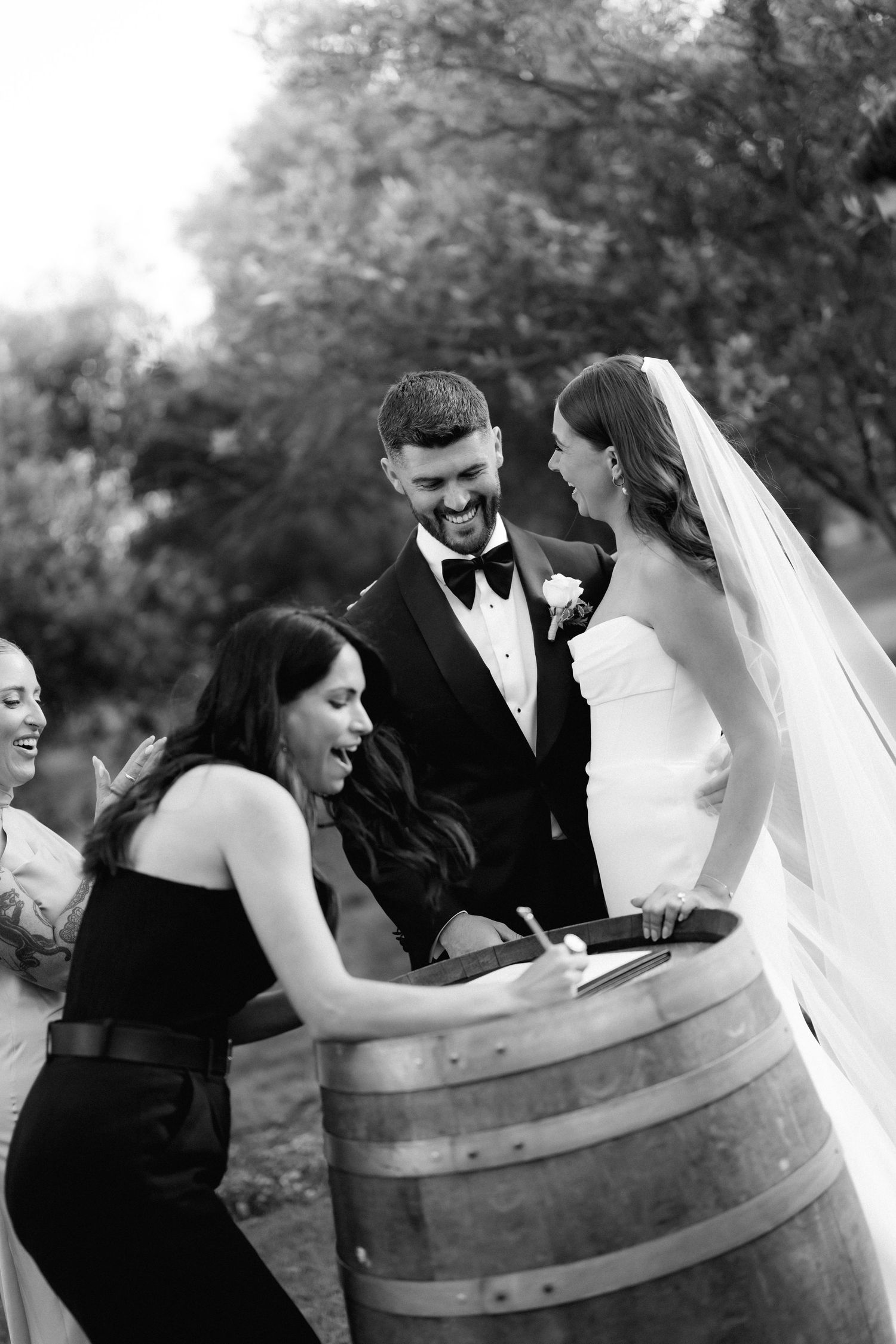 Wedding party posing playfully around wine barrels outdoors.