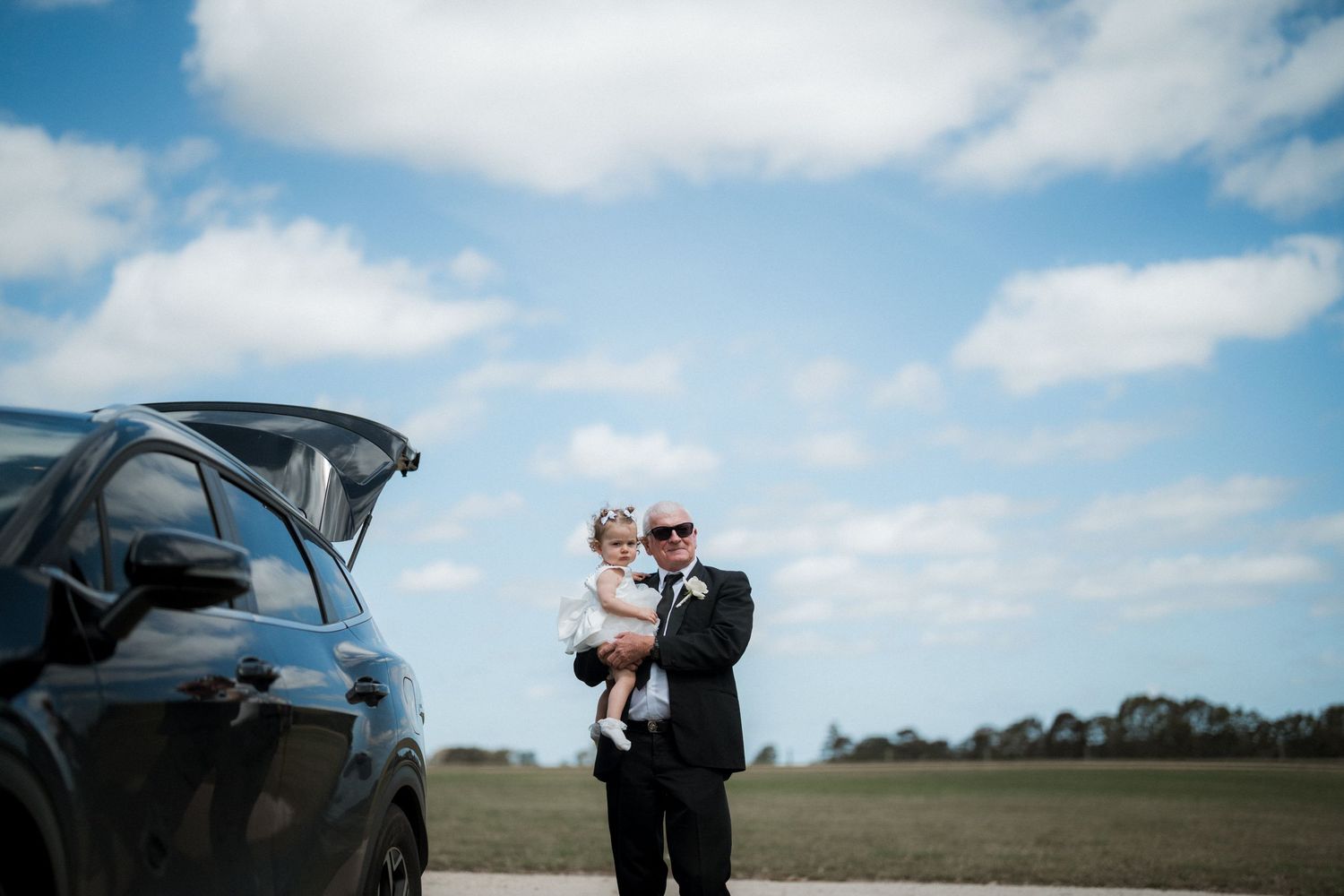 Romantic wedding couple embracing against blue sky and countryside backdrop.