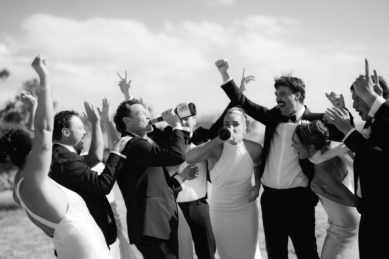 Wedding party members raising their arms in celebration outdoors.