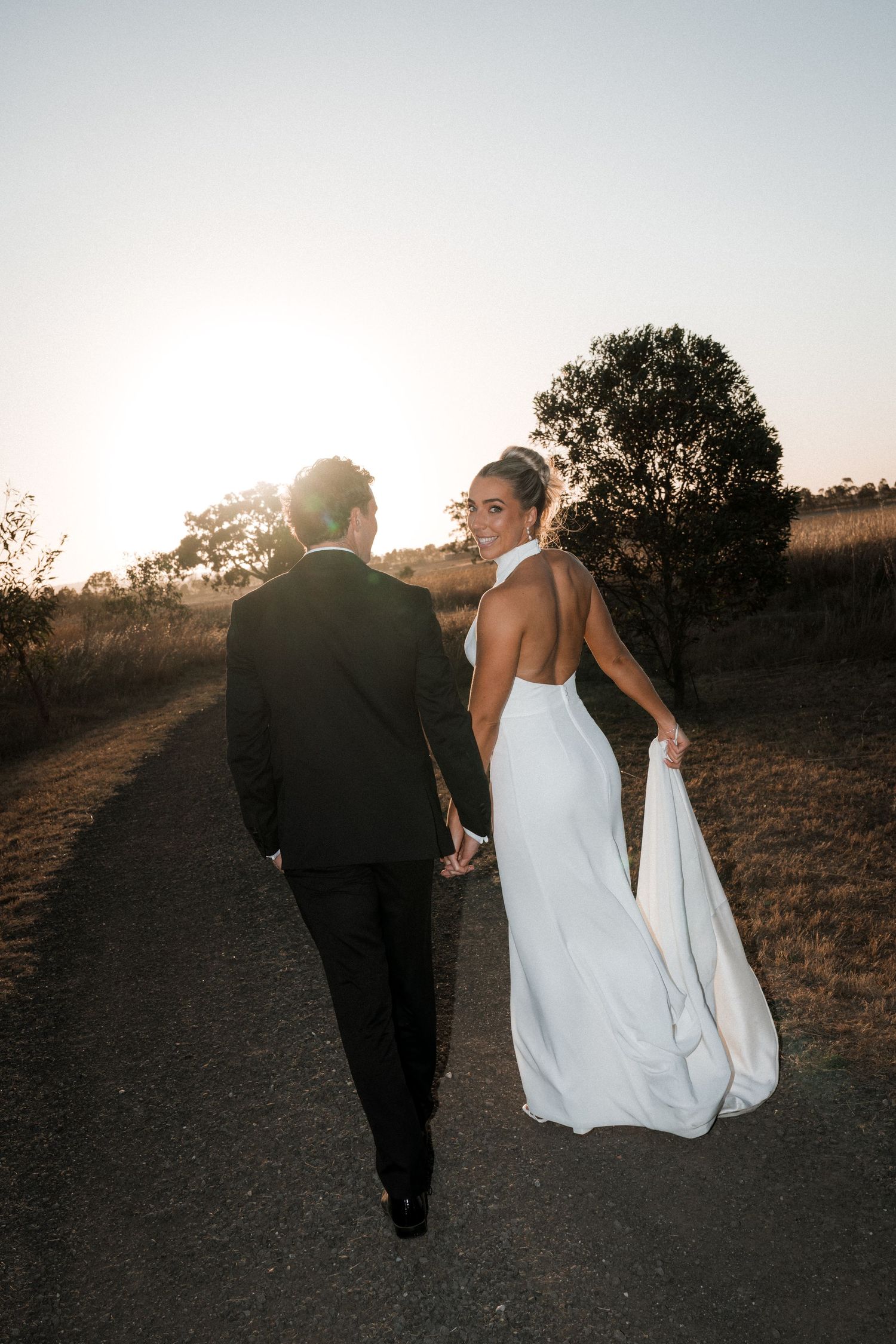Couple walking together on path during sunset after wedding ceremony.