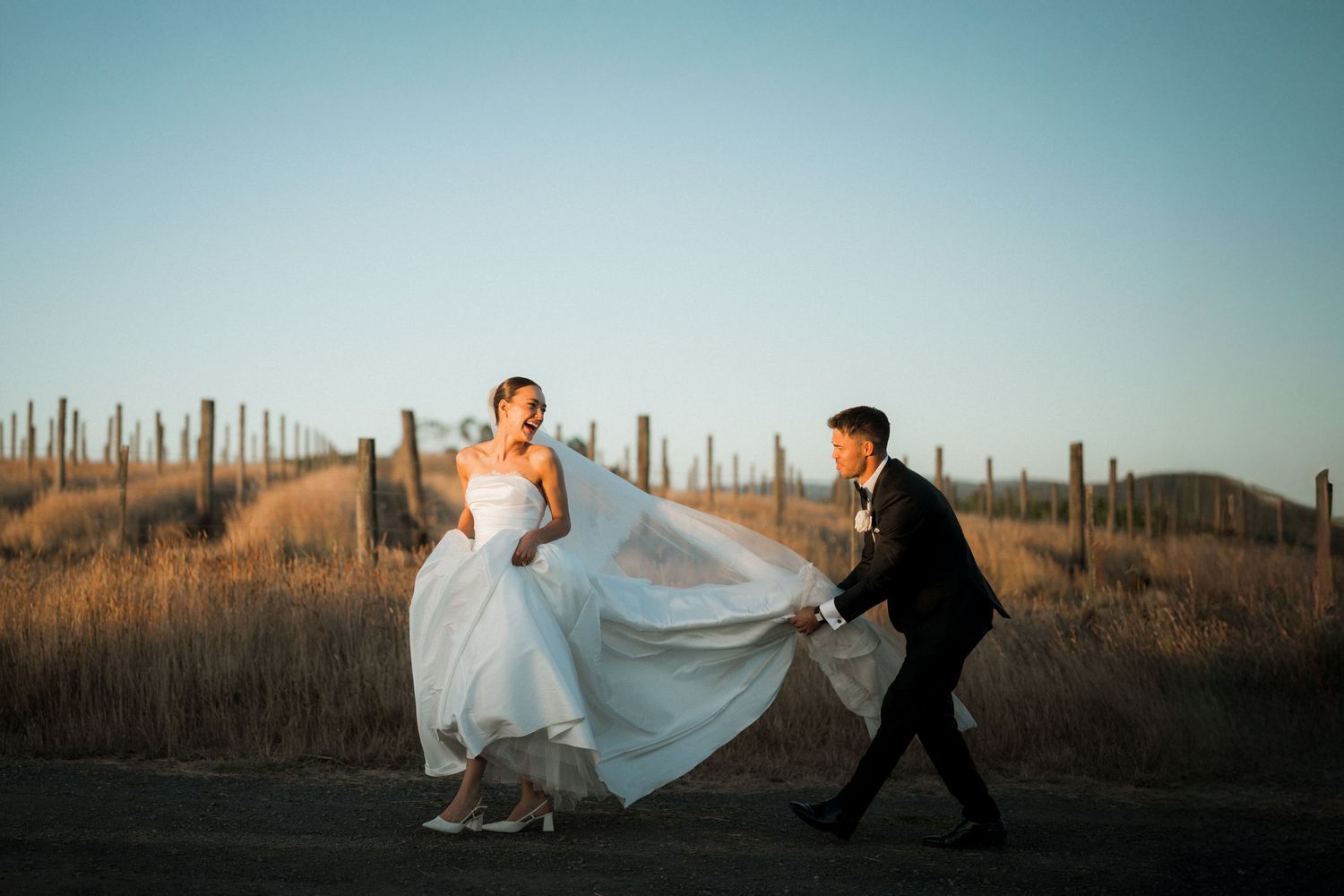 Playful wedding couple runs through desert landscape at sunset with flowing white dress.