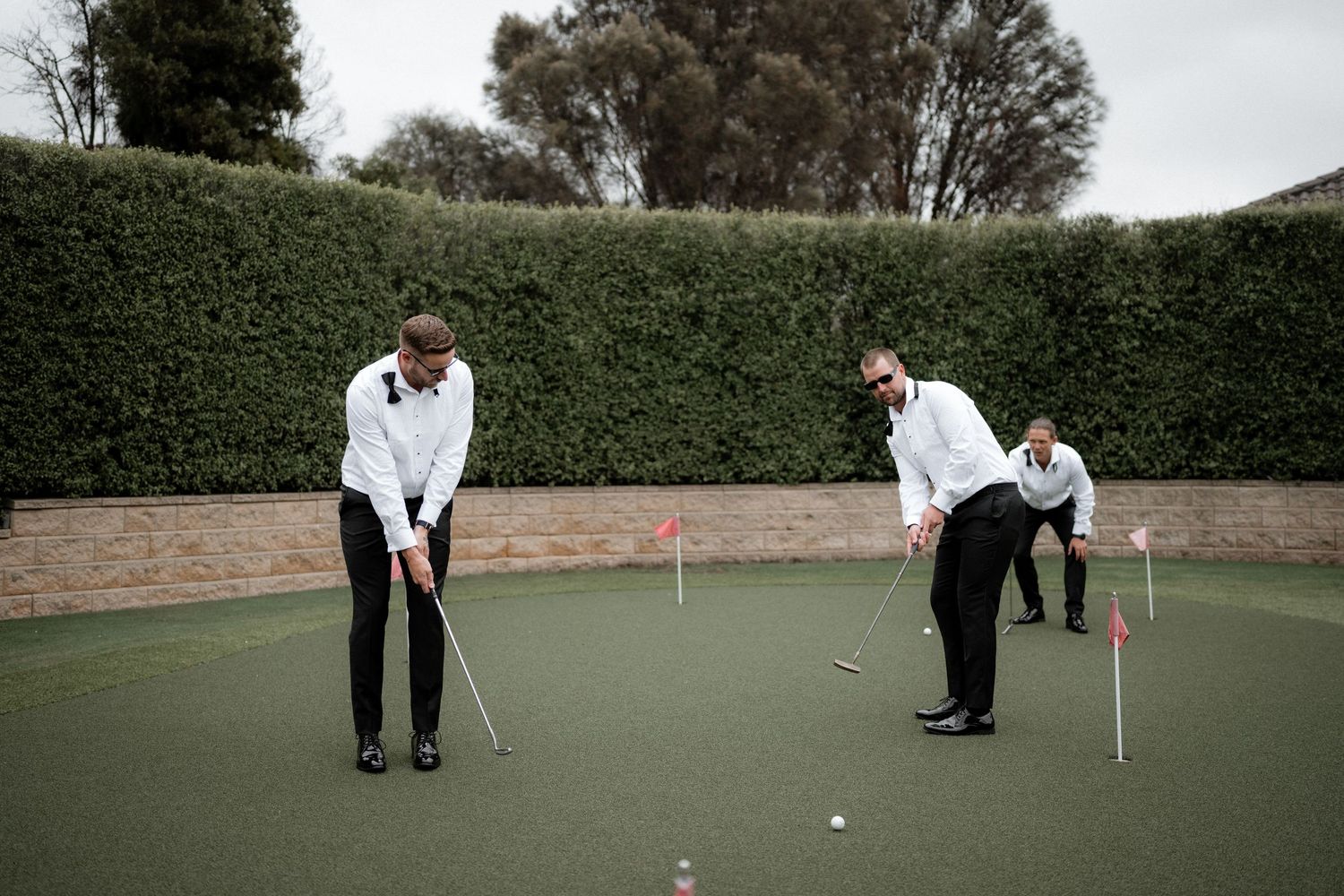 Wedding party members practicing putting on an outdoor golf course.