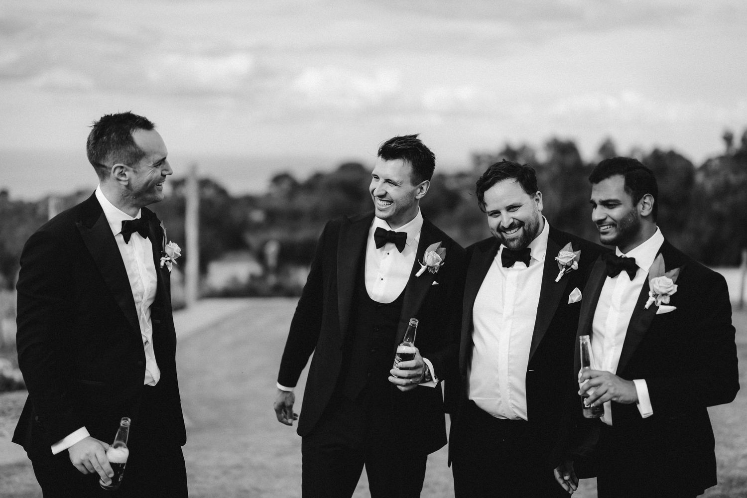 A group of groomsmen in black tuxedos share laughs and conversations during wedding celebrations.