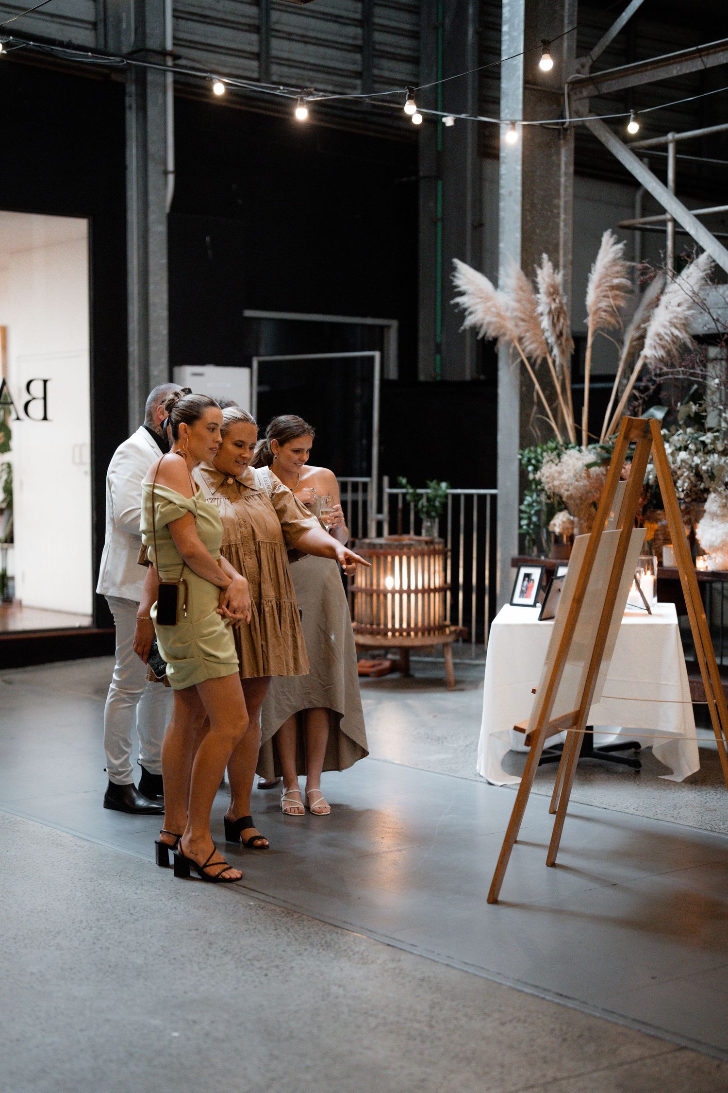 Wedding reception venue setup with wooden easels and pampas grass decorations in an industrial space.