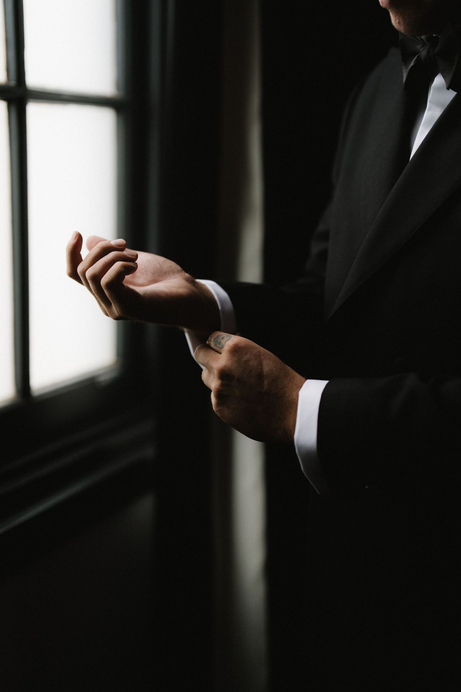 Close-up of groom in black tuxedo adjusting his cufflinks in dramatic lighting.