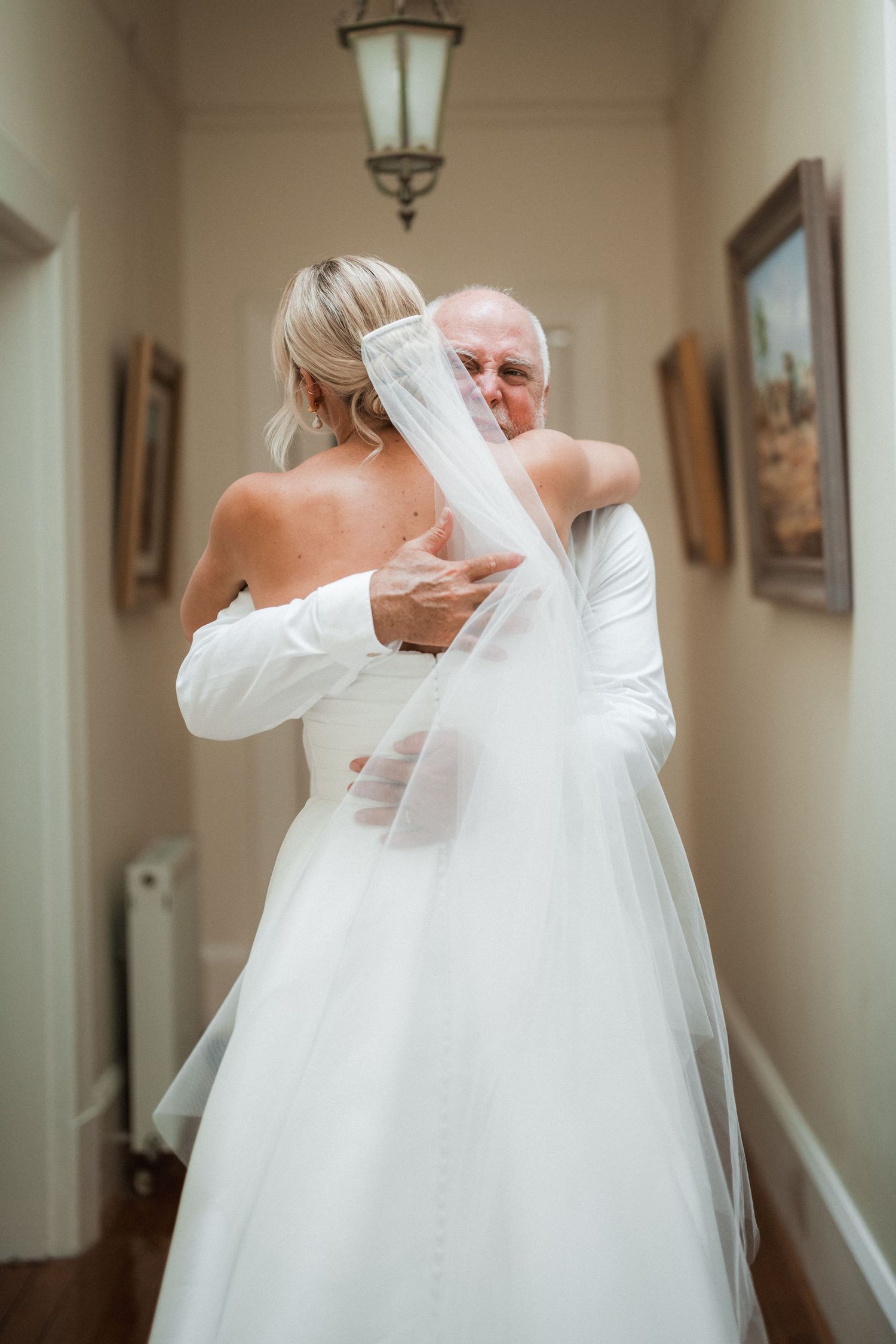 Emotional moment captured in hallway with ornate lamp overhead.