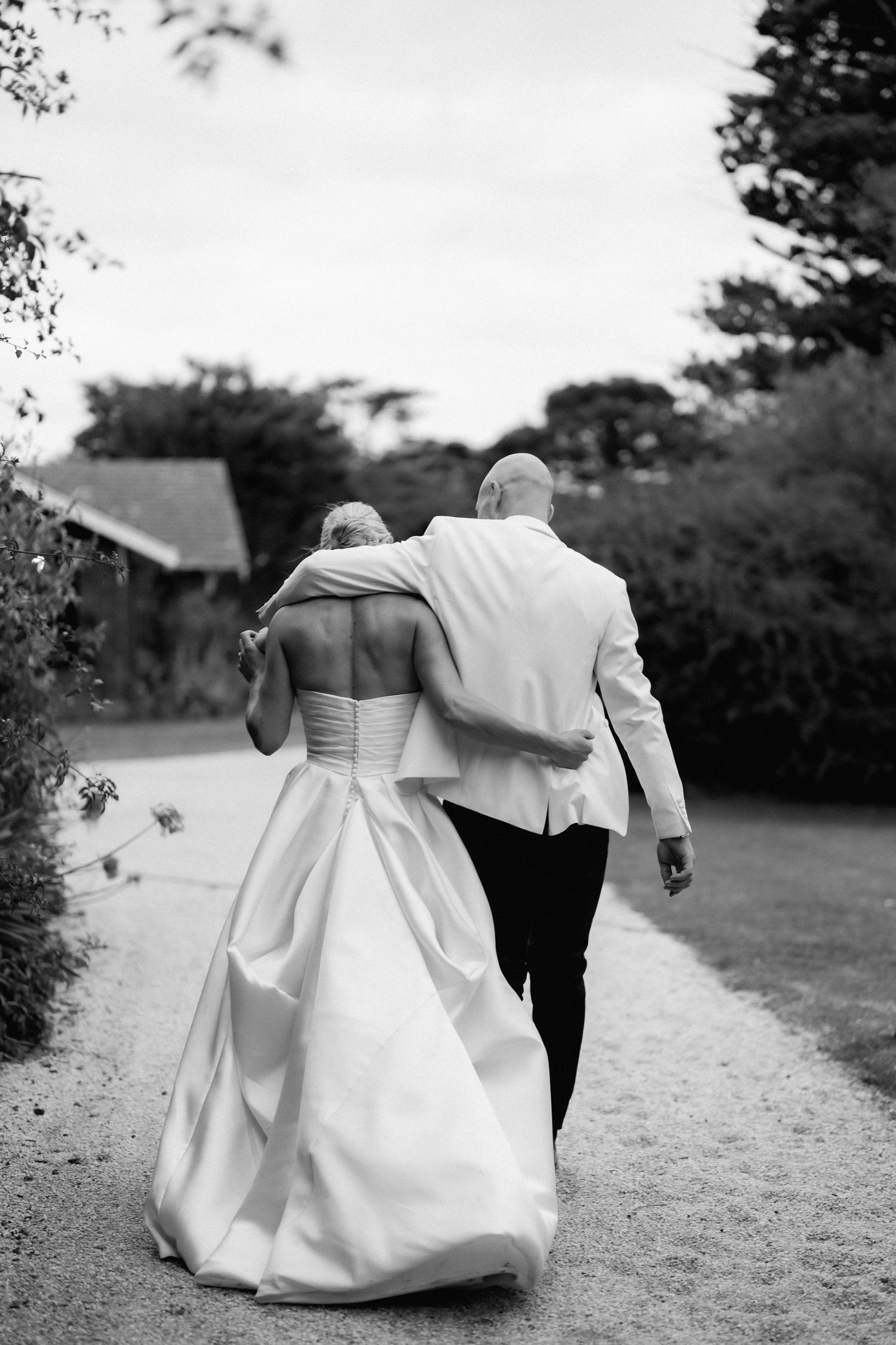 Intimate black and white photo of newlyweds walking away together on garden path.
