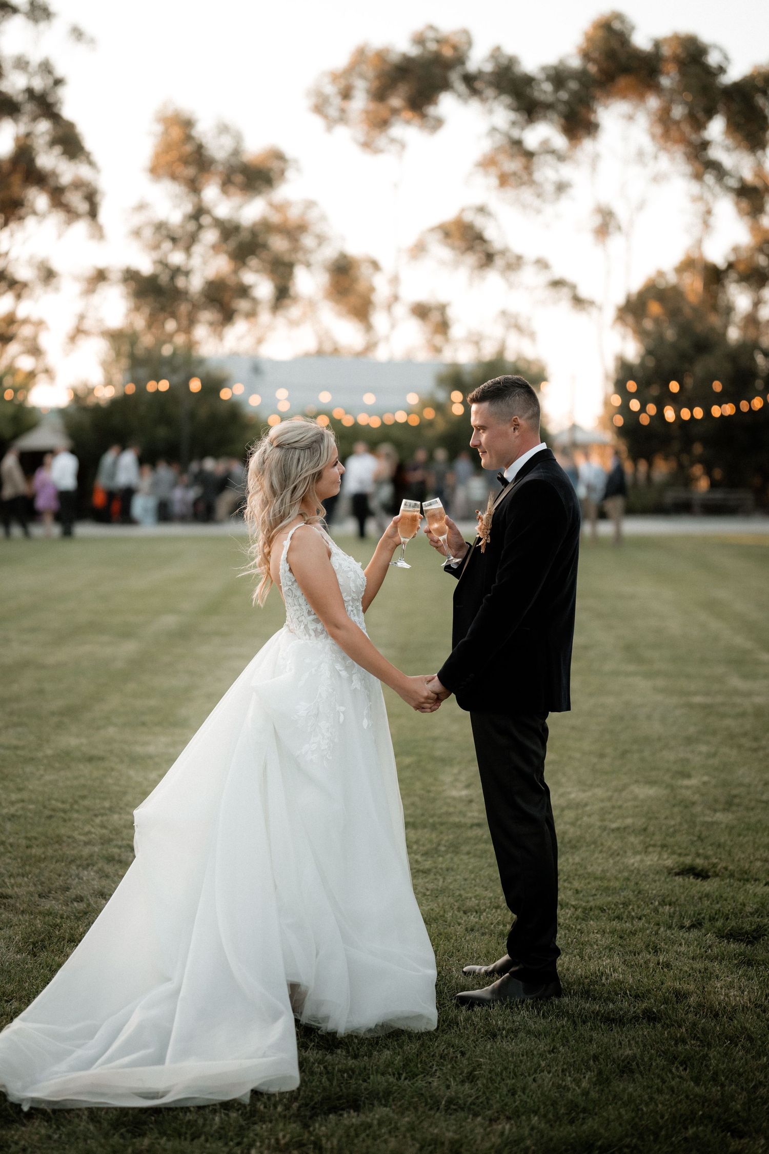 Couple toasts champagne at sunset wedding reception with string lights.