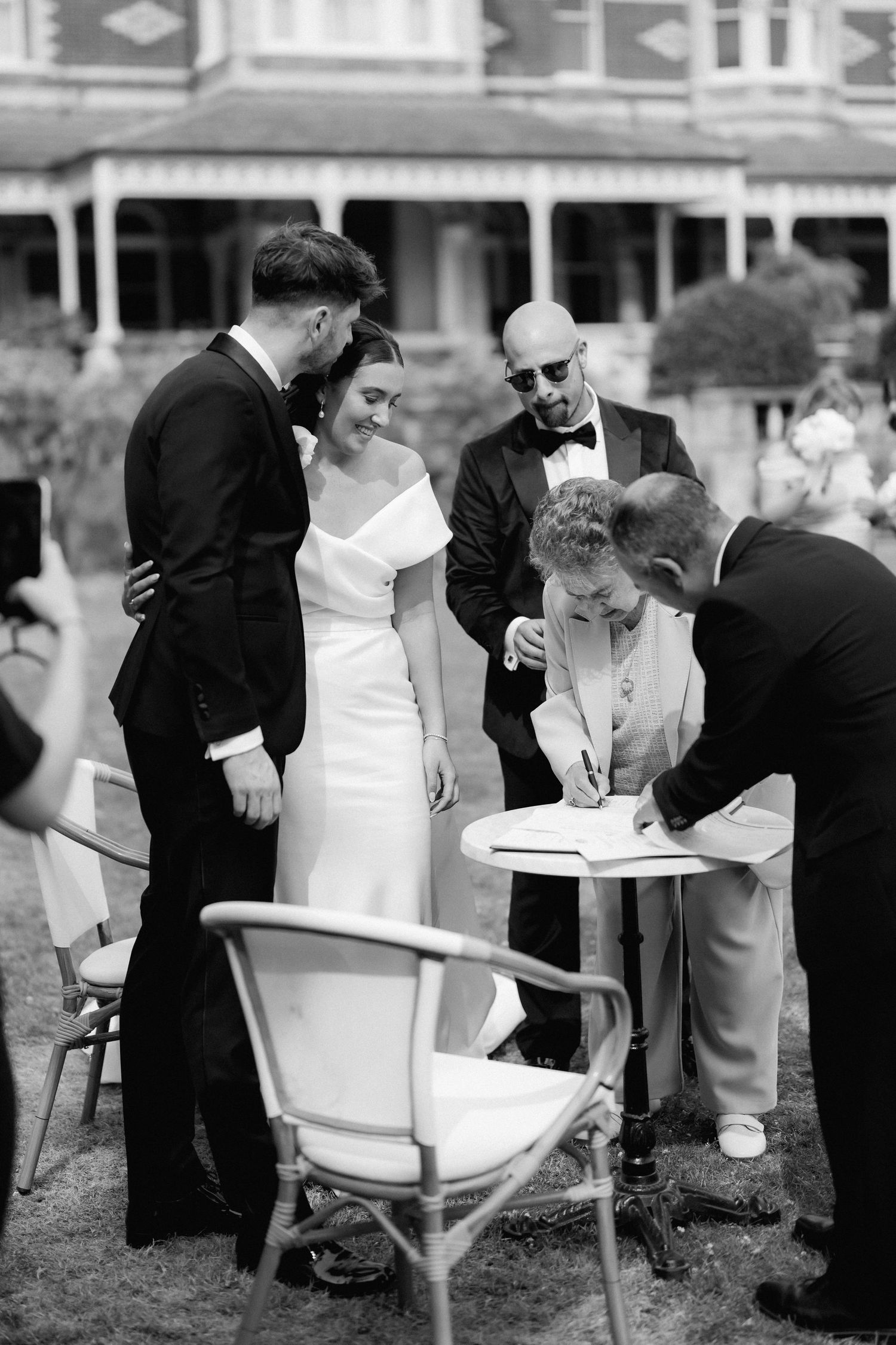 Wedding ceremony guests gather around to sign official documents at an outdoor venue.