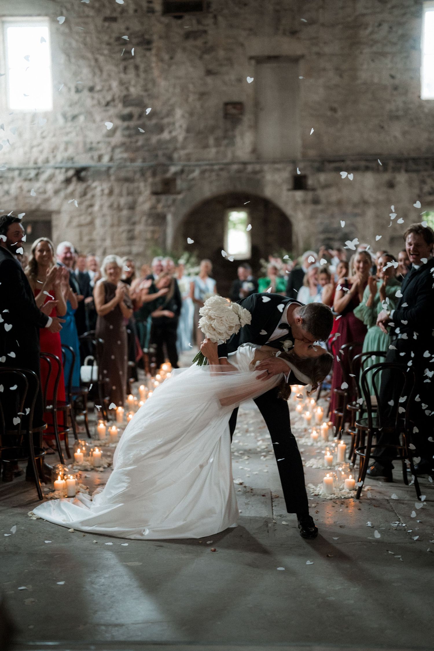 A dramatic first dance in a historic stone venue with guests watching and candlelight creating ambiance.